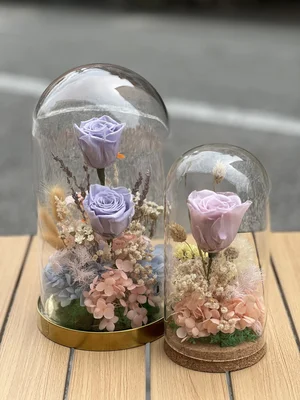 Two glass domes containing preserved lavender and pale pink roses, arranged with dried hydrangeas and filler flowers