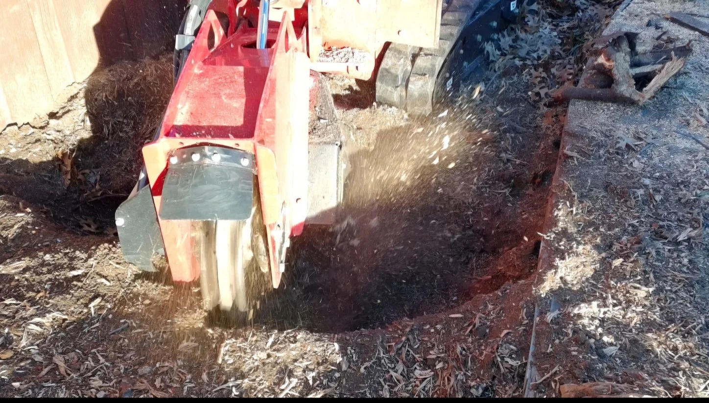 A red and black power tiller cultivates black soil in a garden or farm area, with a wooden fence in the background.
