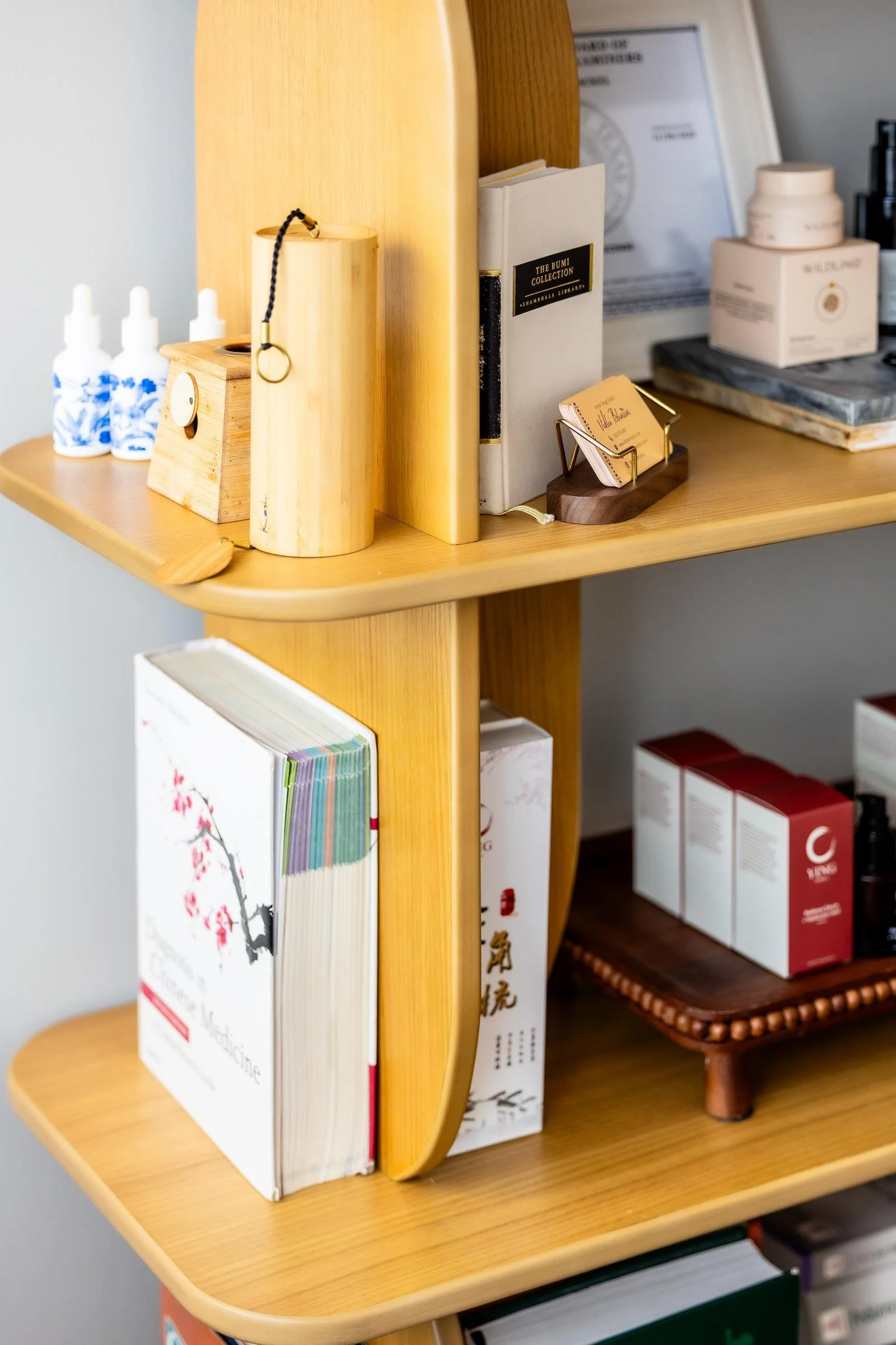 A bookshelves with various books, a business card holder, and some skincare products.