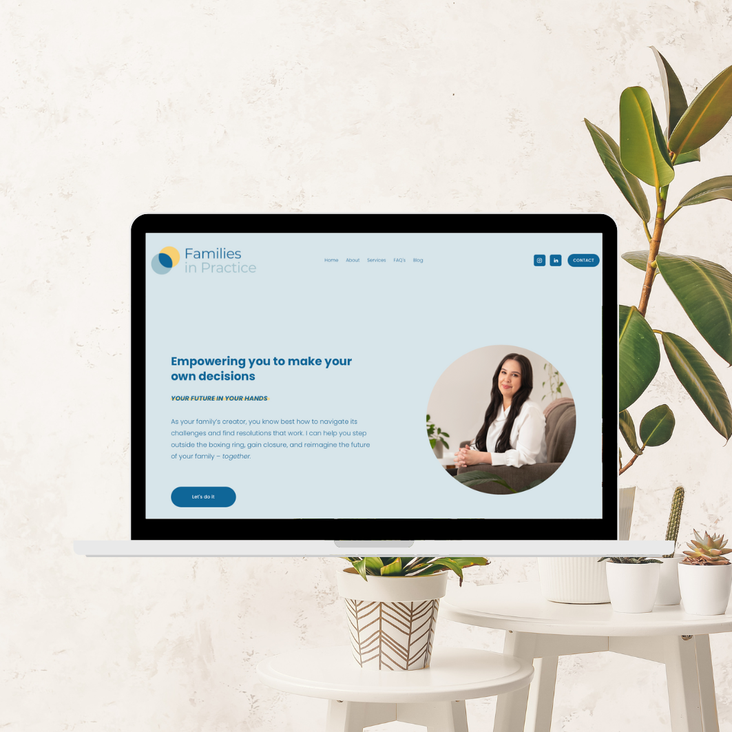 A computer monitor displays a website titled 'Families in Practice,' with a woman sitting on a couch, smiling. The scene includes a white side table with potted plants and a large leafy plant beside the monitor.