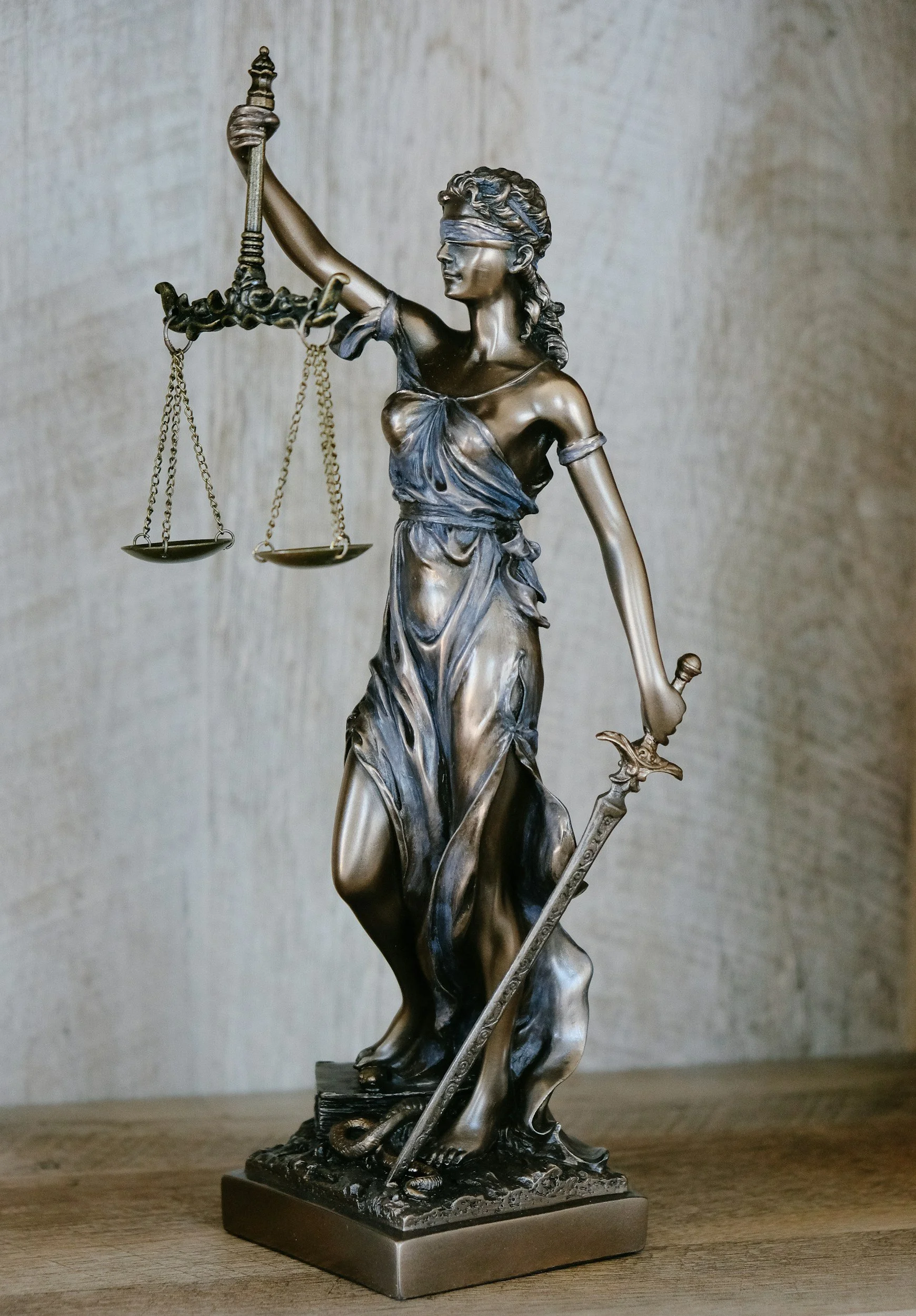 Bronze statue of Lady Justice holding scales and a sword, blindfolded, standing on a wooden surface.