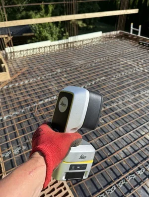 Leica iCS50 instrument held above reinforced concrete slab rebar mesh before pour — digital layout on a formwork site