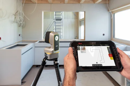 Leica iCS50 instrument on carbon tripod with operator holding tablet showing the iCON field software — kitchen fit-out layout in progress