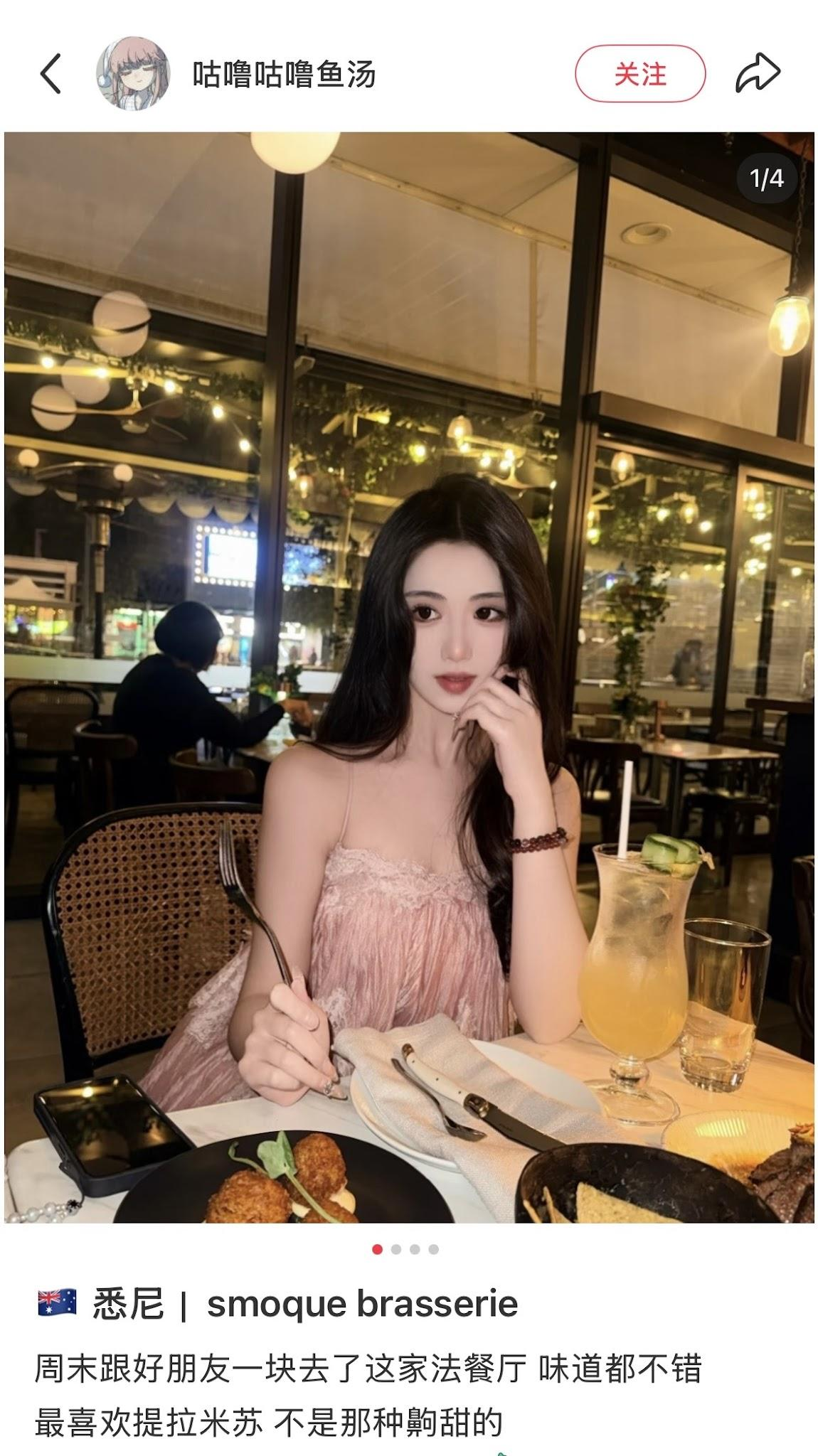 A woman with dark hair wearing a pink dress sitting at a restaurant table with food and drinks, including a macaron, fried appetizers, and a cocktail with lime slices, in a warmly lit indoor setting.
