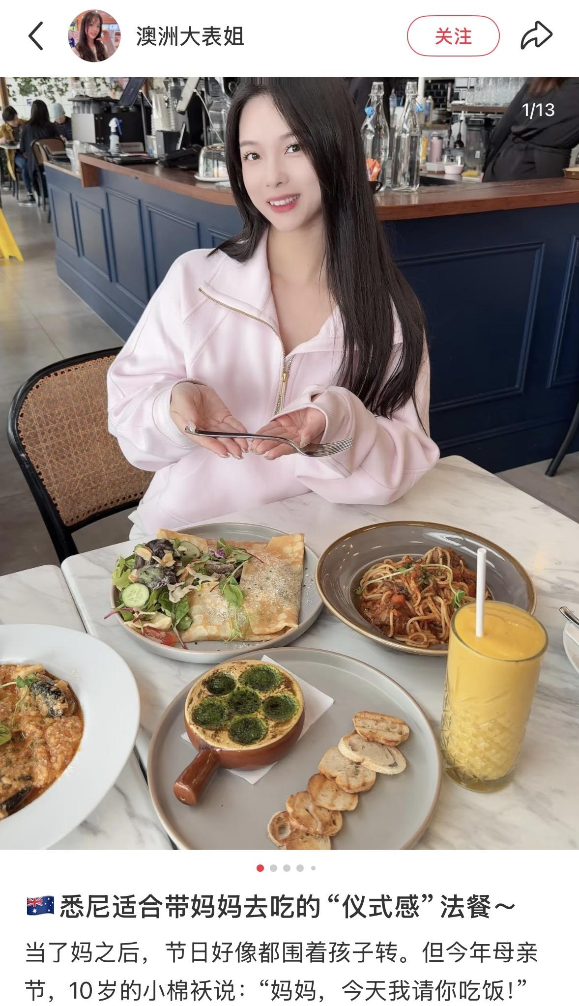 A woman at a restaurant with a variety of dishes on the table, including salad, pasta, and desserts, smiling and holding a fork.