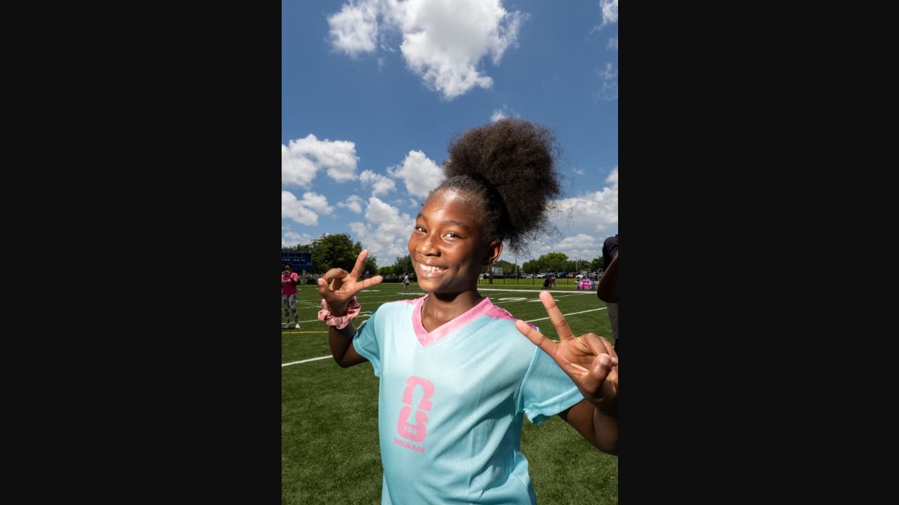 Girl at a CREW football event wearing a pink-trimmed bib and giving two peace signs, photographed by Timeless Productions