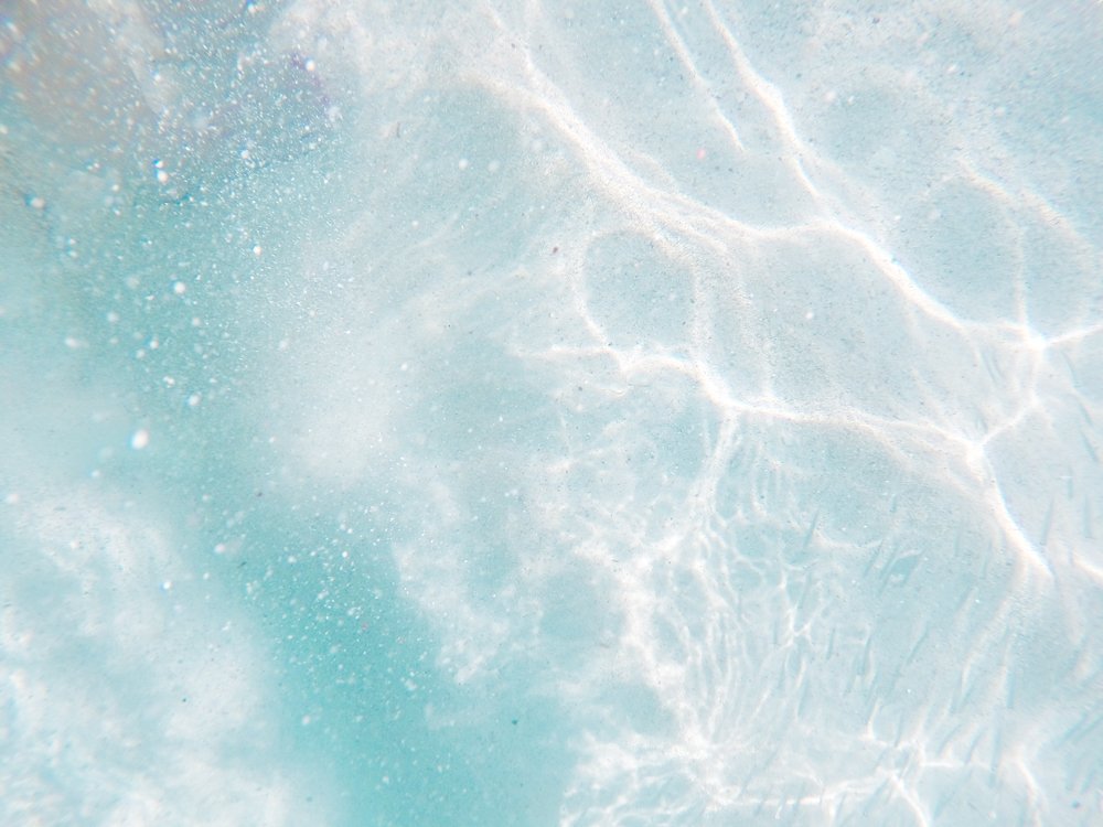 Underwater view of a swimming pool with sunlight reflections and bubbles
