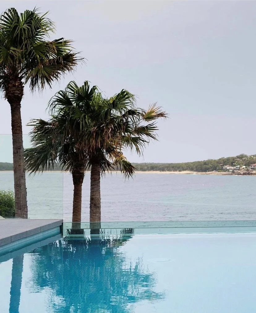 Swimming pool with a view of the ocean and palm trees in the background.