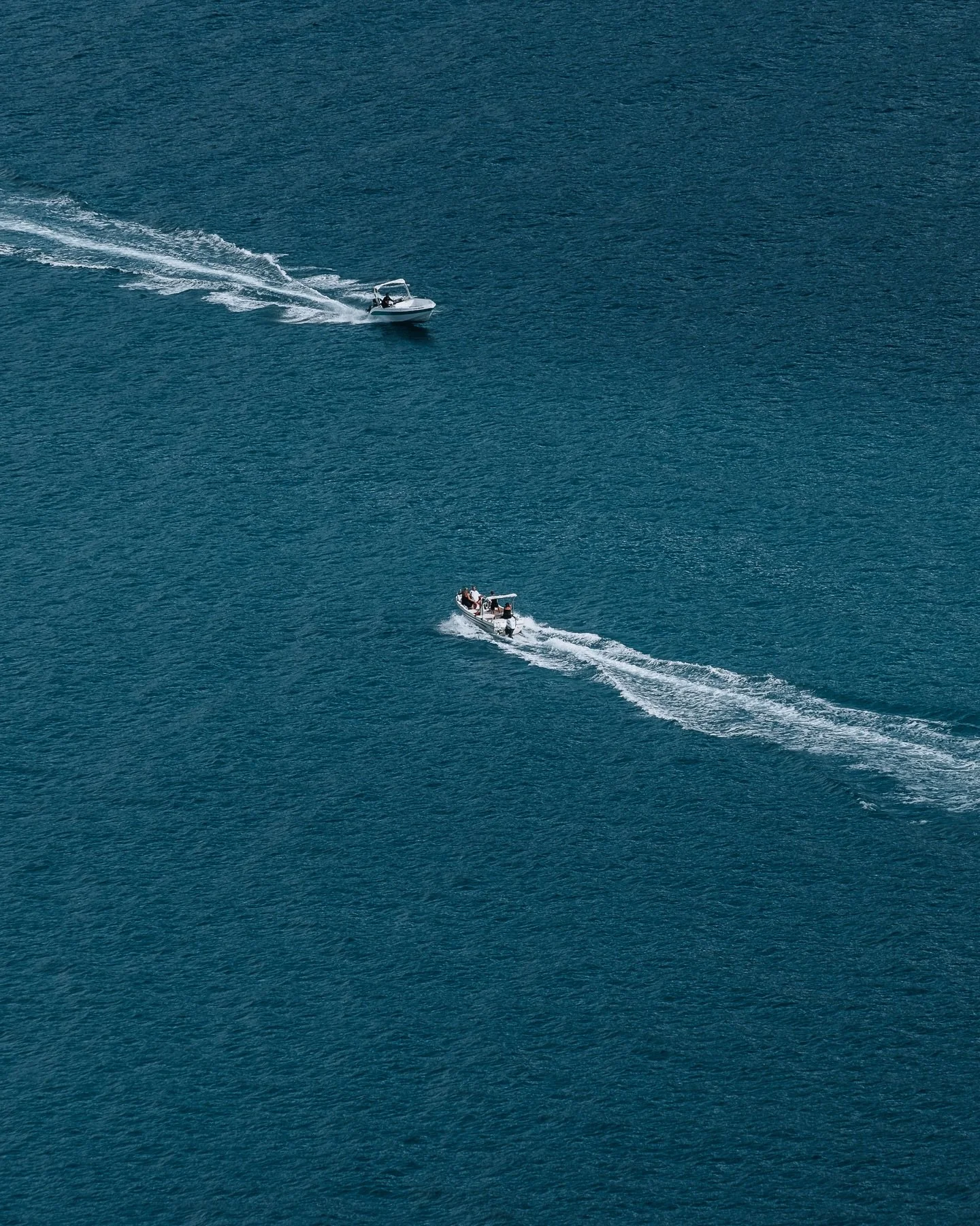 Two speedboats cut across the ocean, their white wakes crossing like quick signatures.

Up close, it must have felt urgent.
Demanding. Directional.

But from above, nothing is broken.
The sea holds the crossing without resistance.

Equilibrium isn&rs