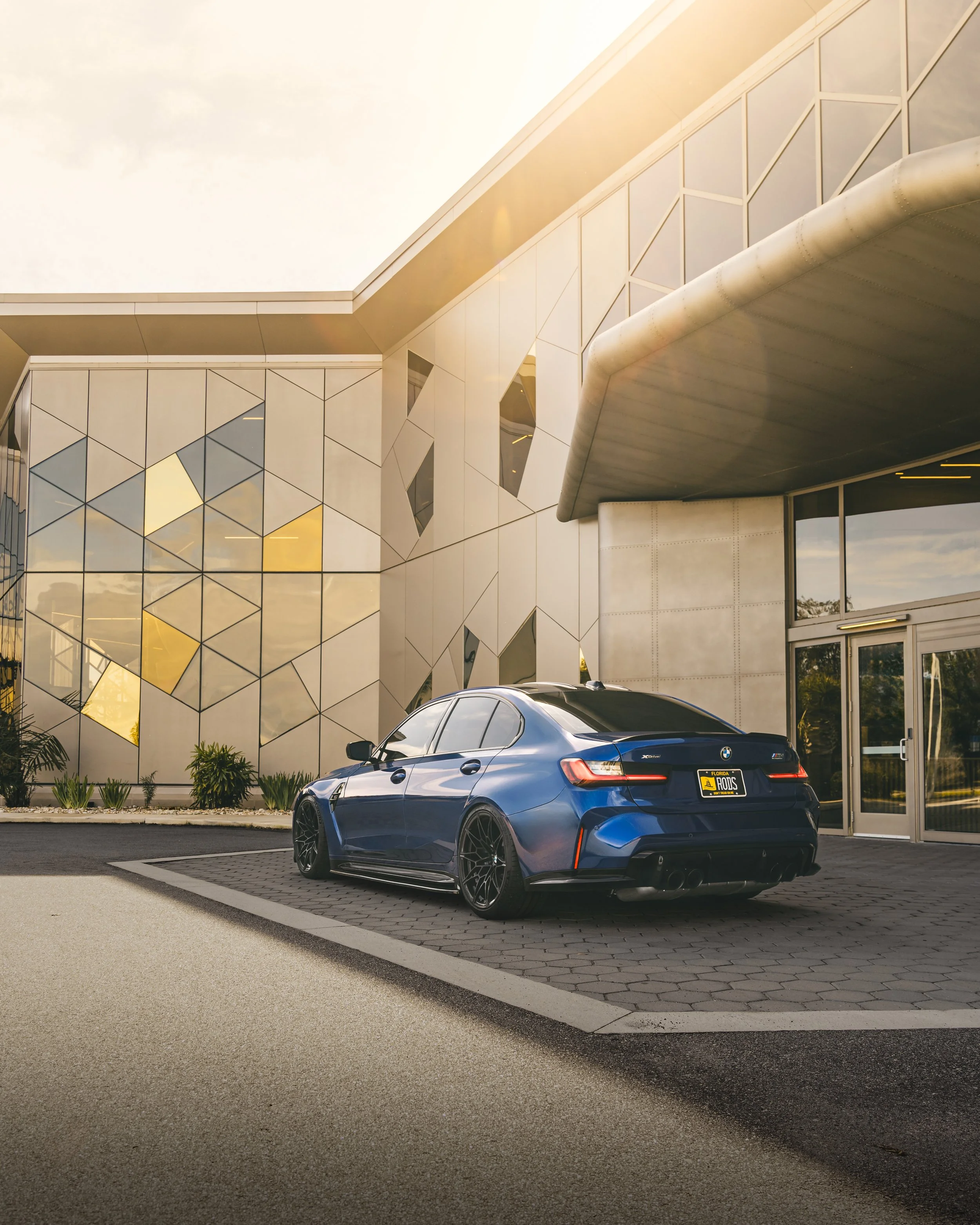 A blue modern sedan parked in front of a contemporary building with geometric glass and metal design