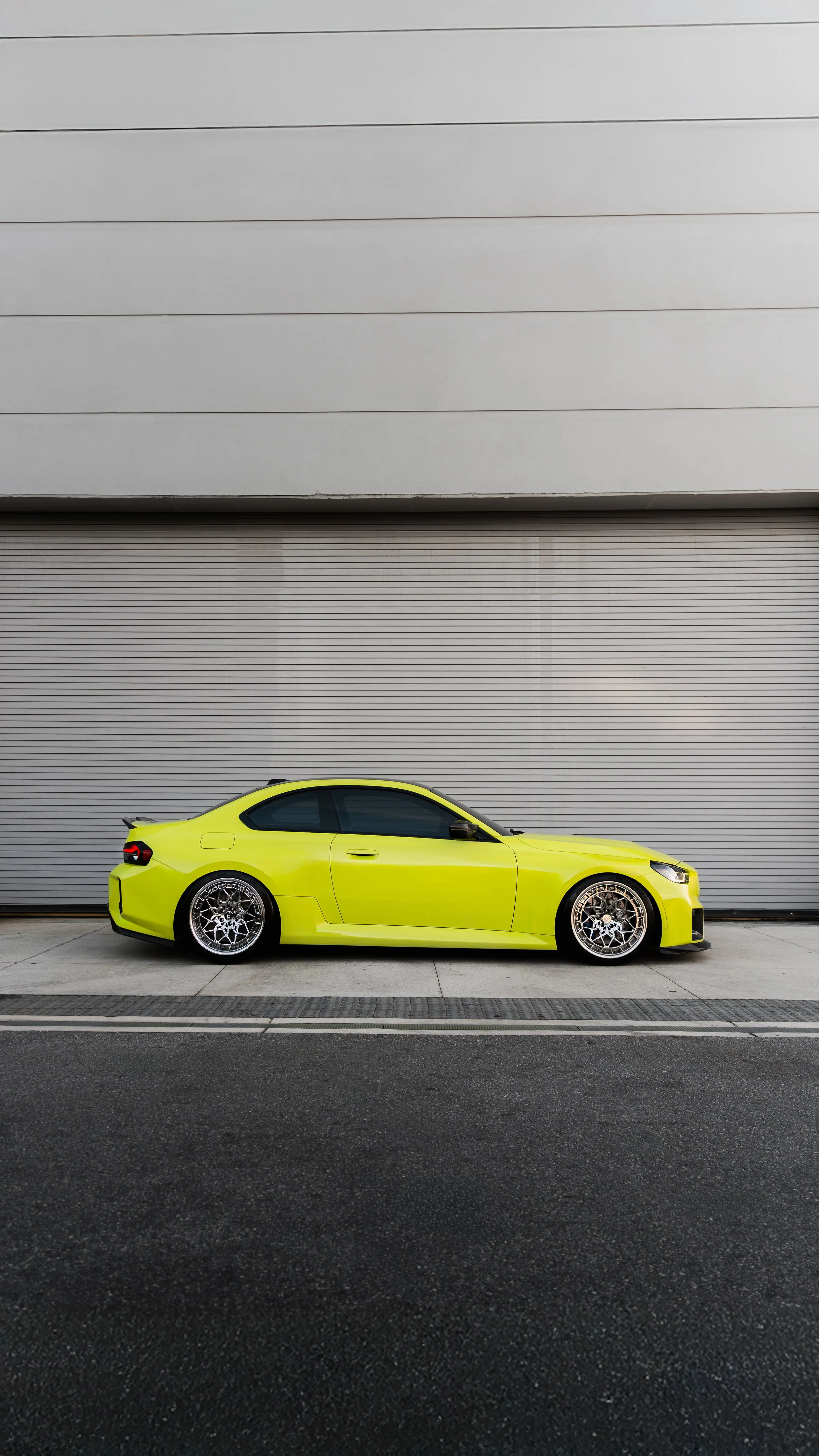 A yellow sports car parked in front of a gray industrial building with a large rolling door
