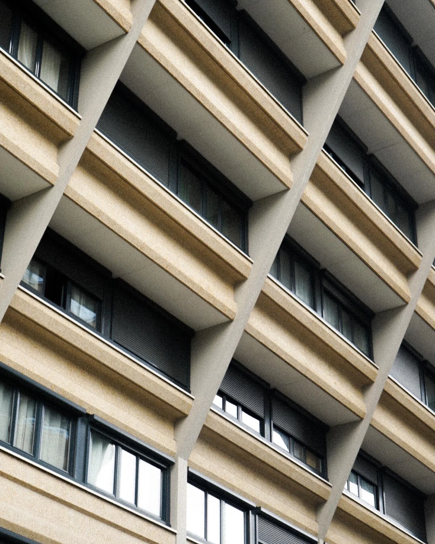 Close-up view of a modern multi-story building with repeating beige and gray concrete balconies and evenly spaced windows.