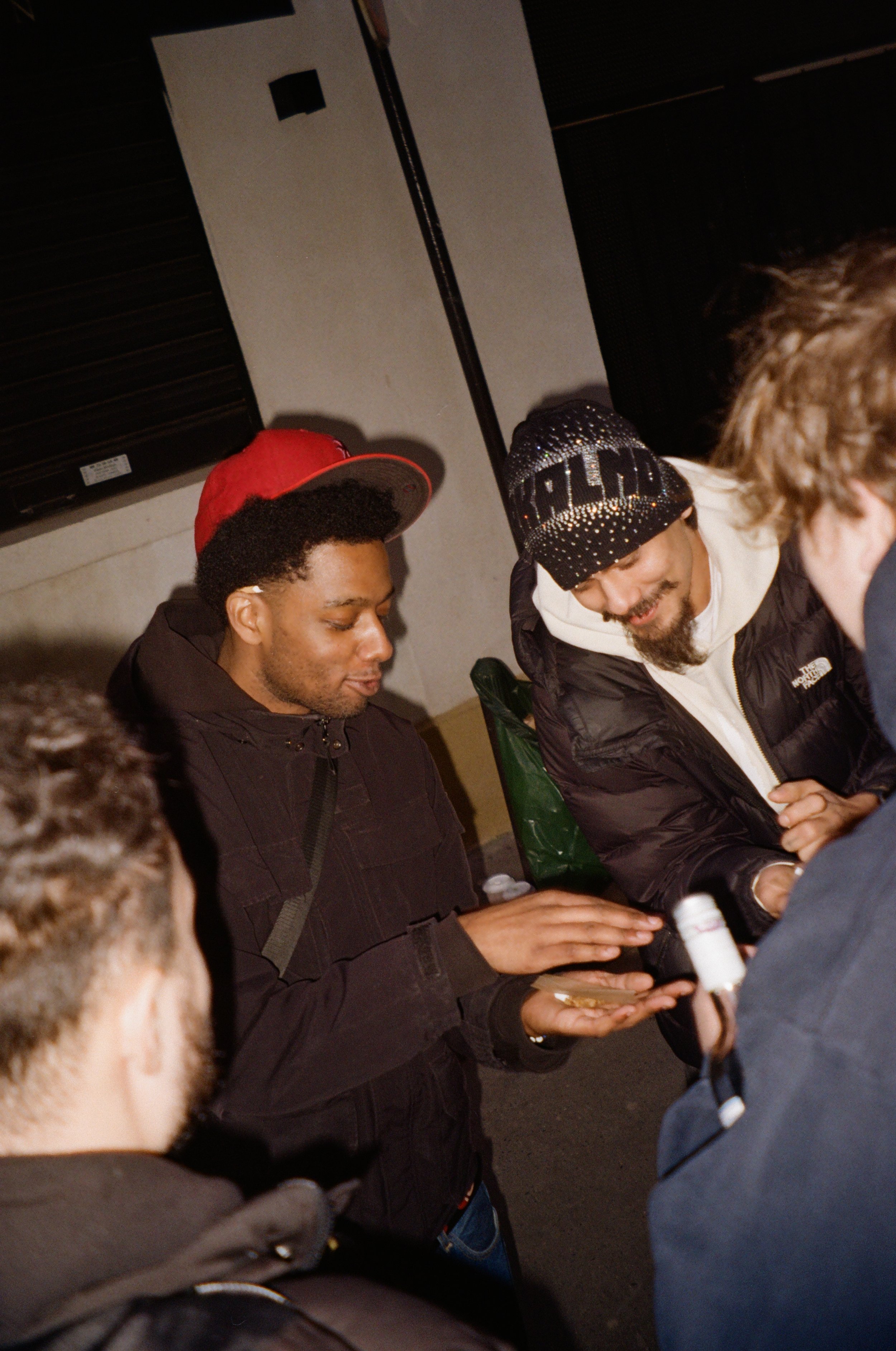 Group of young men gathered outdoors, engaged in conversation, one showing something on his phone, others smiling and listening.