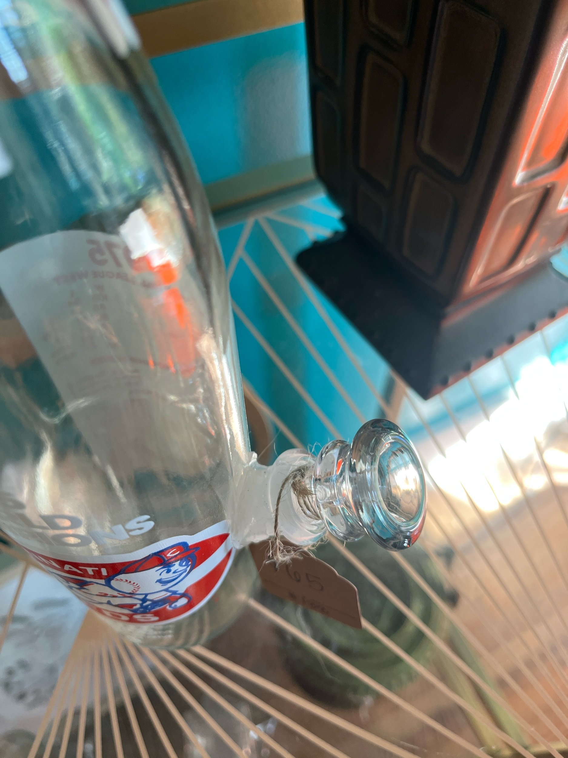 Vintage Cincinnati Reds Pepsi bottle turned into a water pipe, with a close up of the bowl, displayed on a table by a plant.