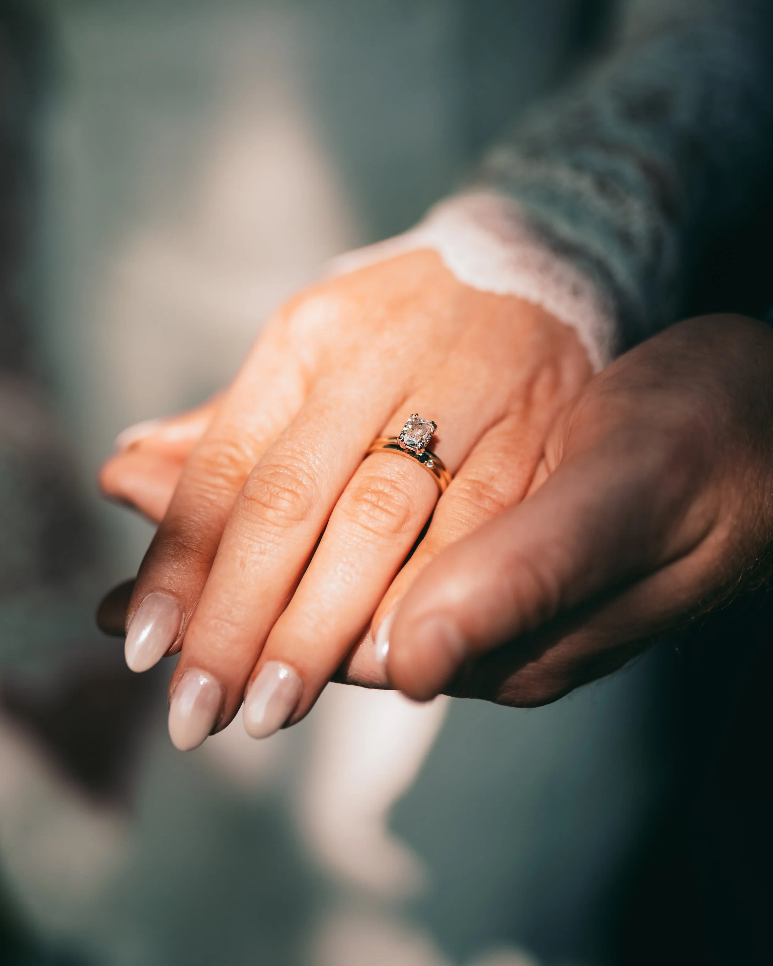 Close-up of a woman's hand wearing an engagement ring with a large diamond, being held by a man's hand.