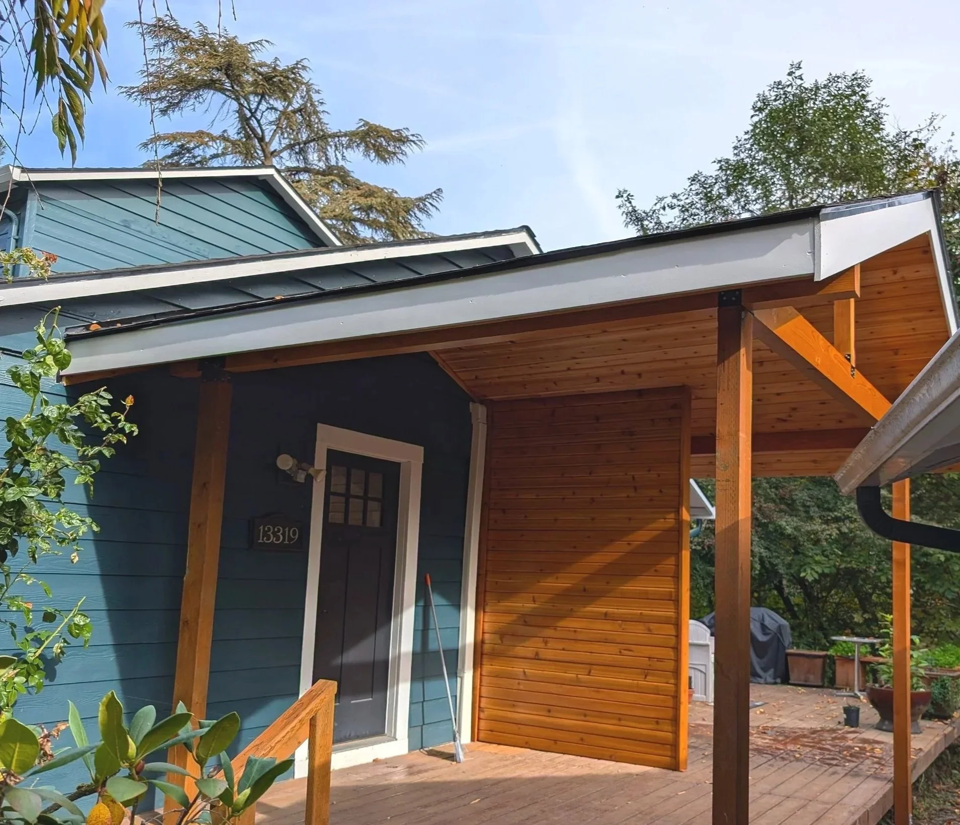 Expertly crafted front porch overhang with bead board and wood siding, surrounded by trees and plants.