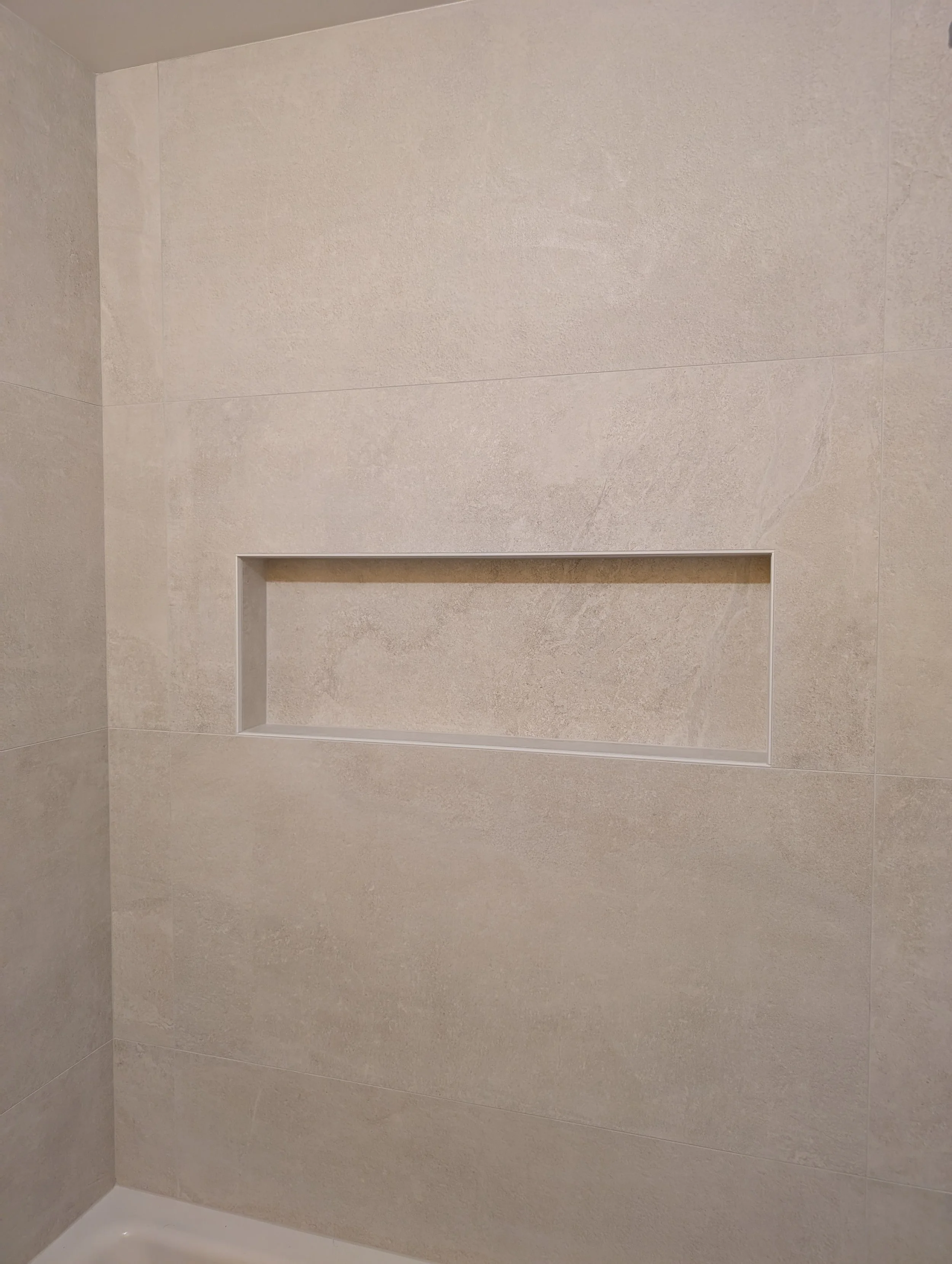 A remodeled shower with expertly tiled wall with a recessed niche in the shower area.