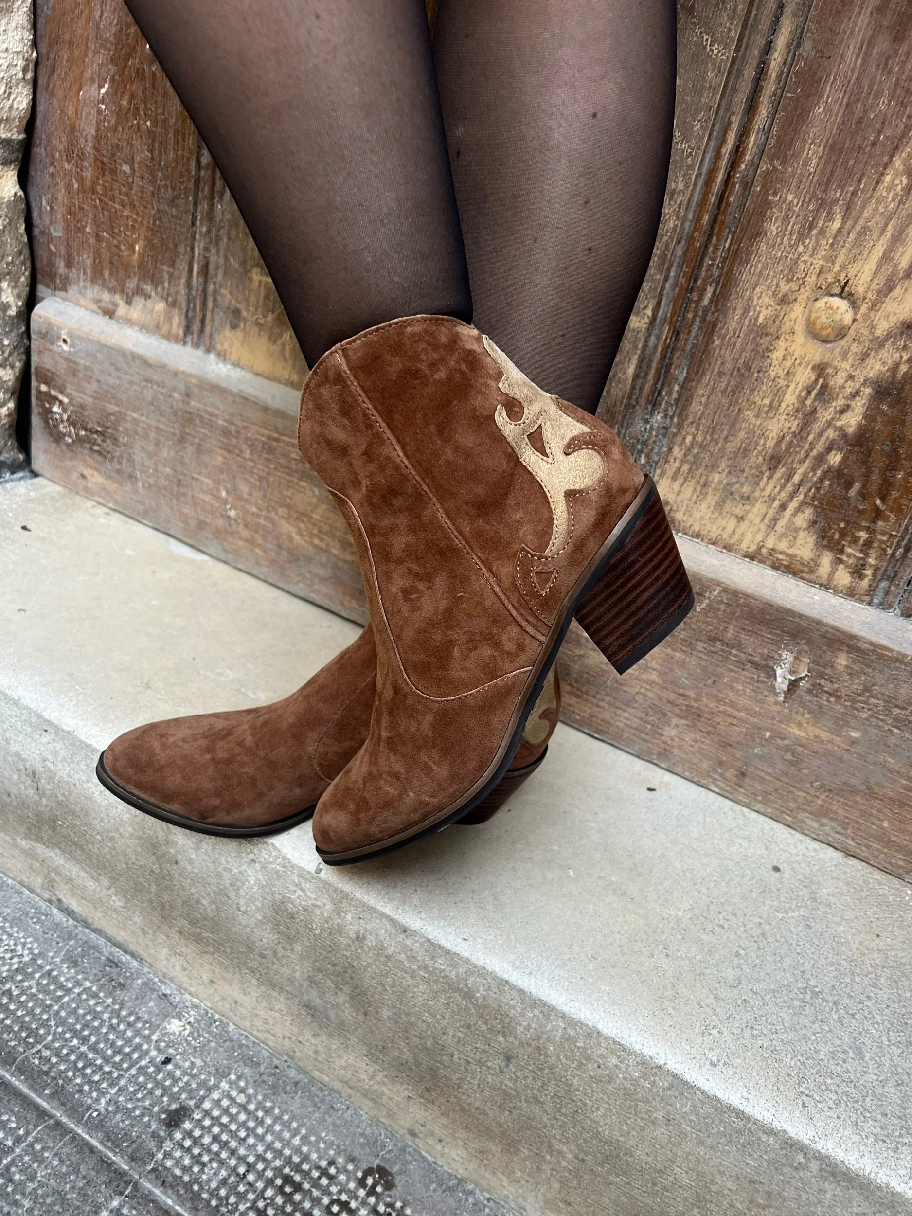Chaussettes noires avec des bottes en suède marron clair, à talons, posées contre une porte en bois.