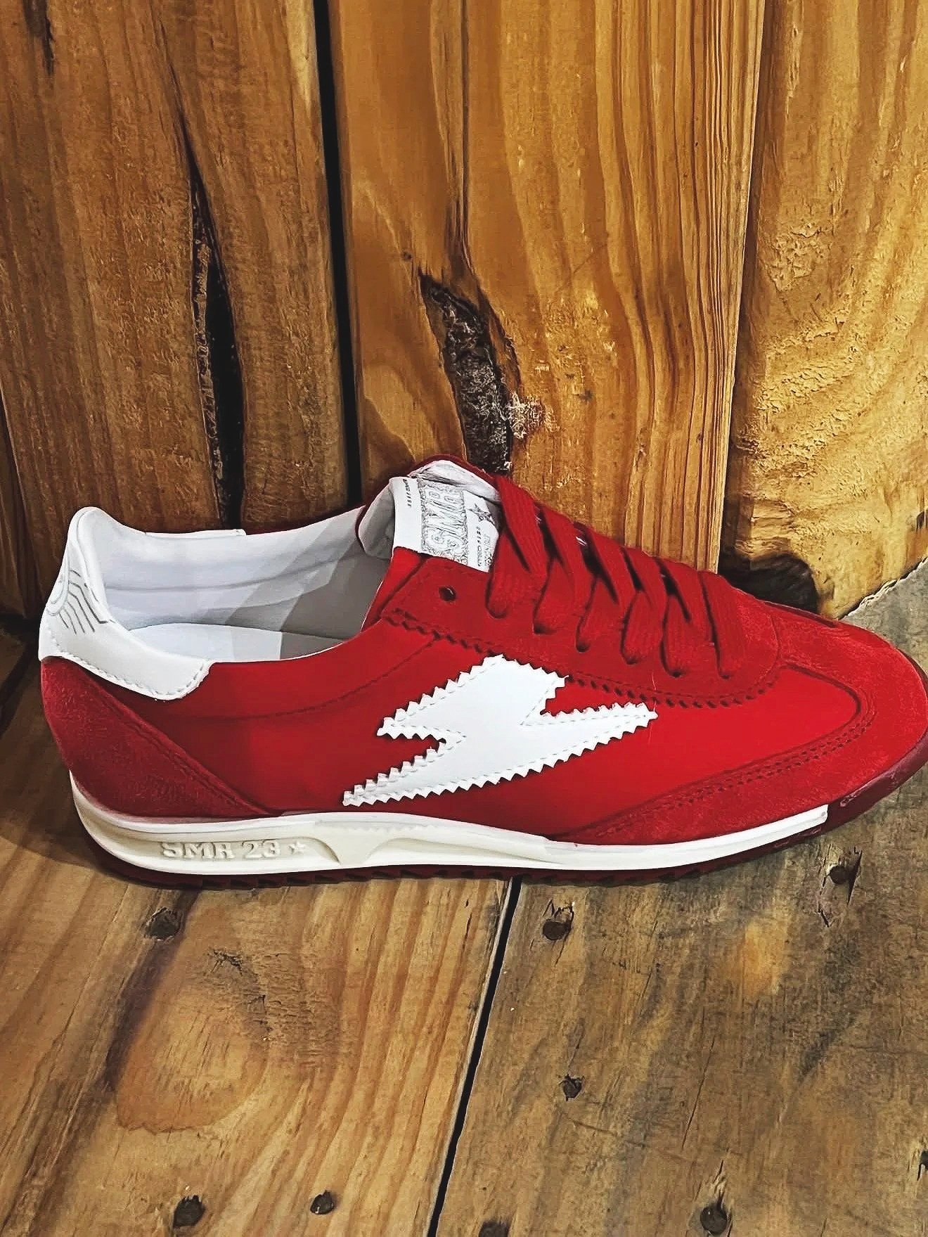 Une chaussure de course rouge avec une grande étoile blanche sur le côté, posée sur un plancher en bois.