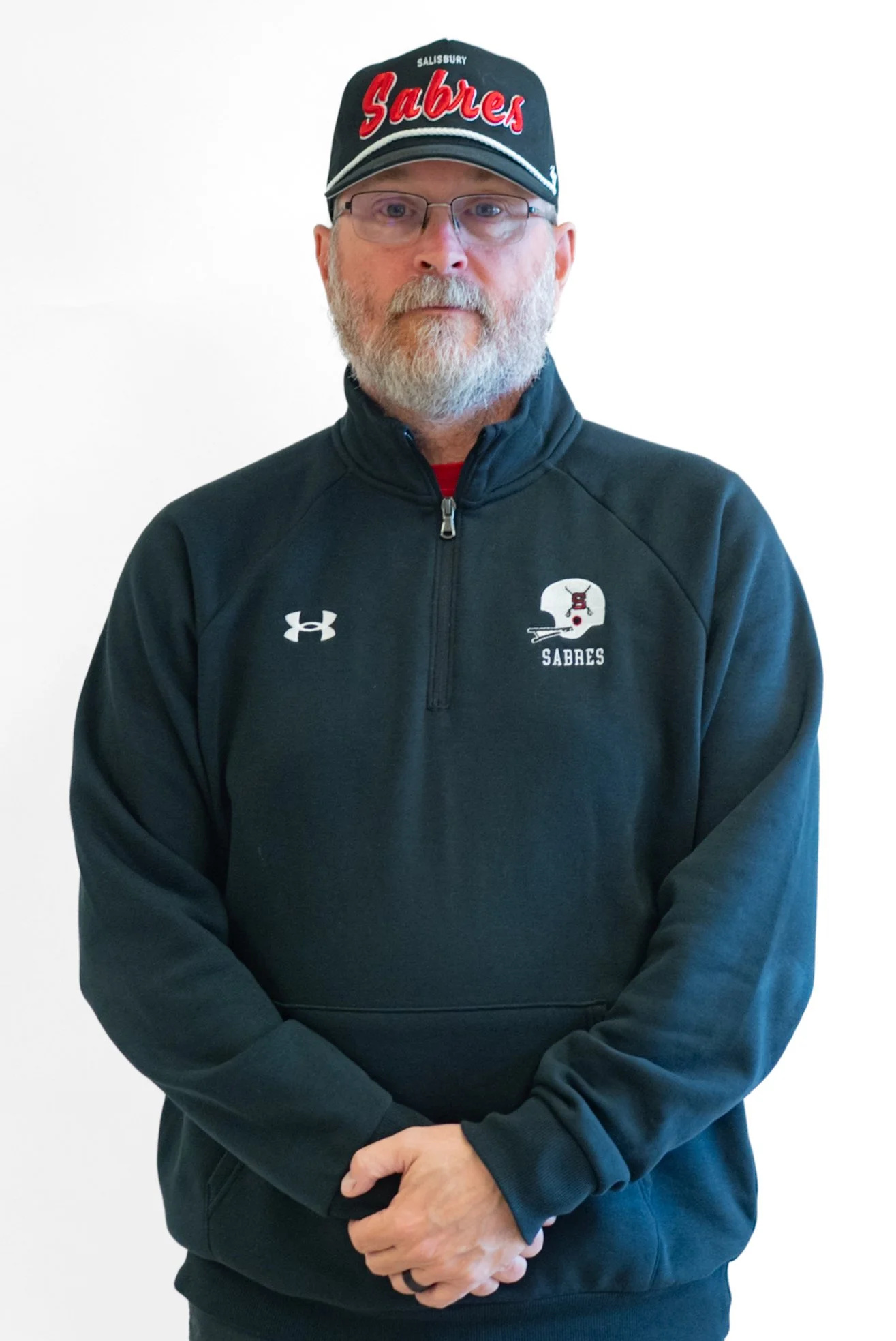 Black and white photo of a man with a beard, wearing a SAL Football jacket, standing against a brick wall.