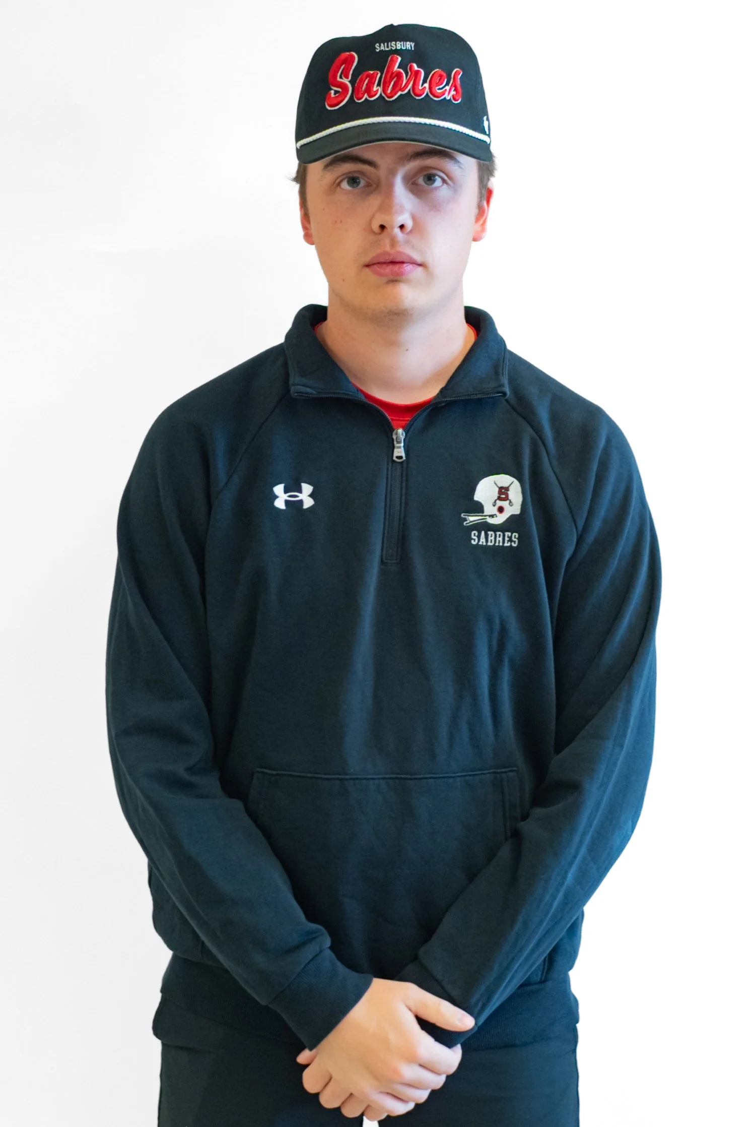 Black and white portrait of a young man smiling, wearing a SAL Football jacket, standing in front of a brick wall.