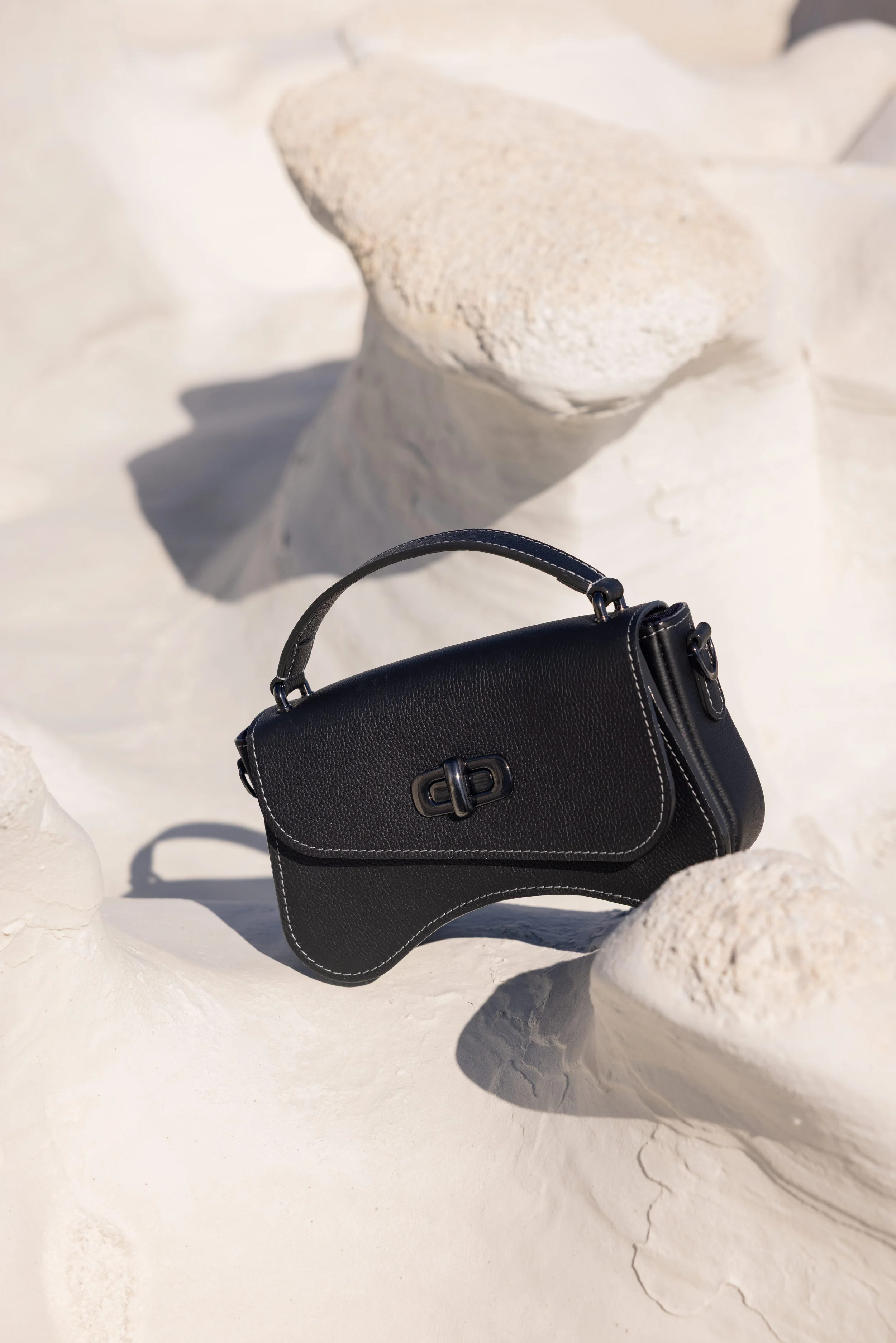 Sac en cuir noir posé sur une roche minérale dans un décor lunaire