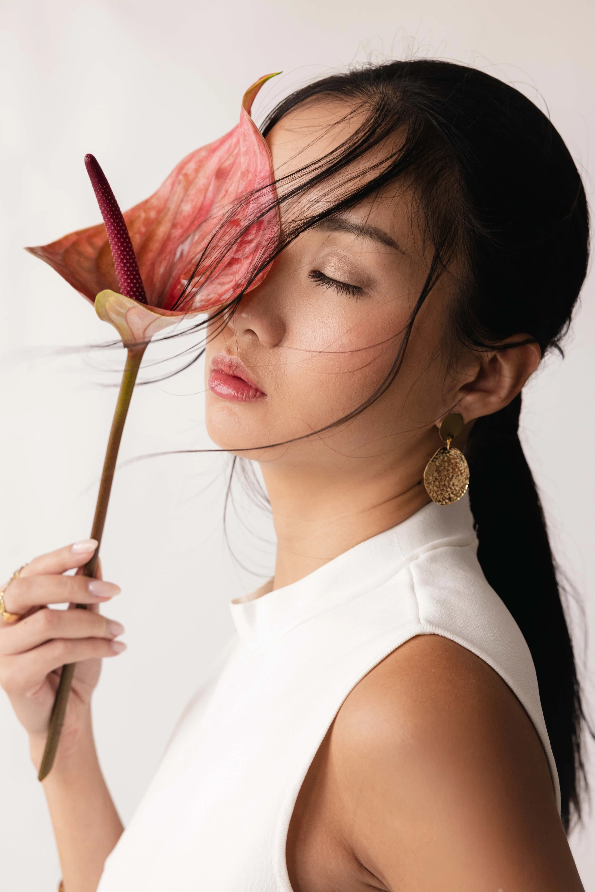 Portrait épuré d'une mannequin avec une fleur rouge sur son visage et une boucle dorée
