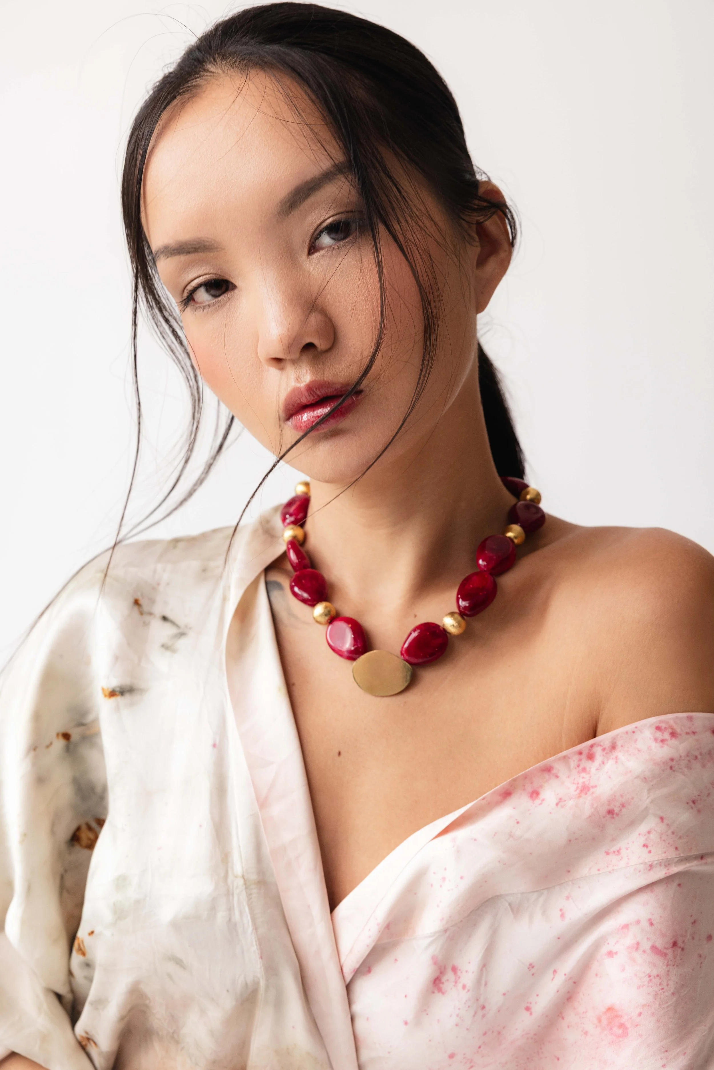 Portrait d'une mannequin en kimono sur fond blanc et portant un collier en pierres rouges