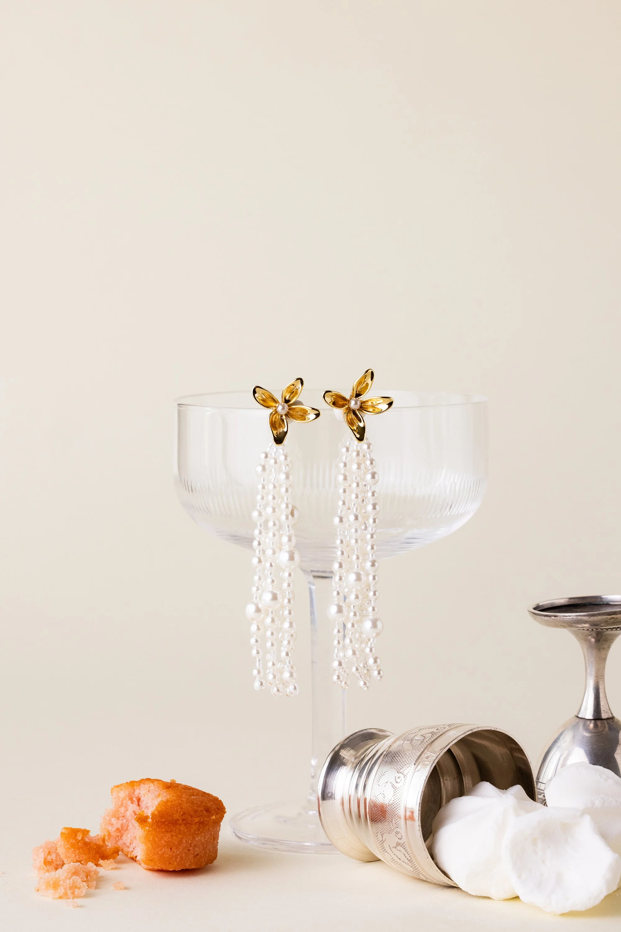 Nature morte d'une paire de boucles en perles posée sur le rebord d'un verre sur fond neutre