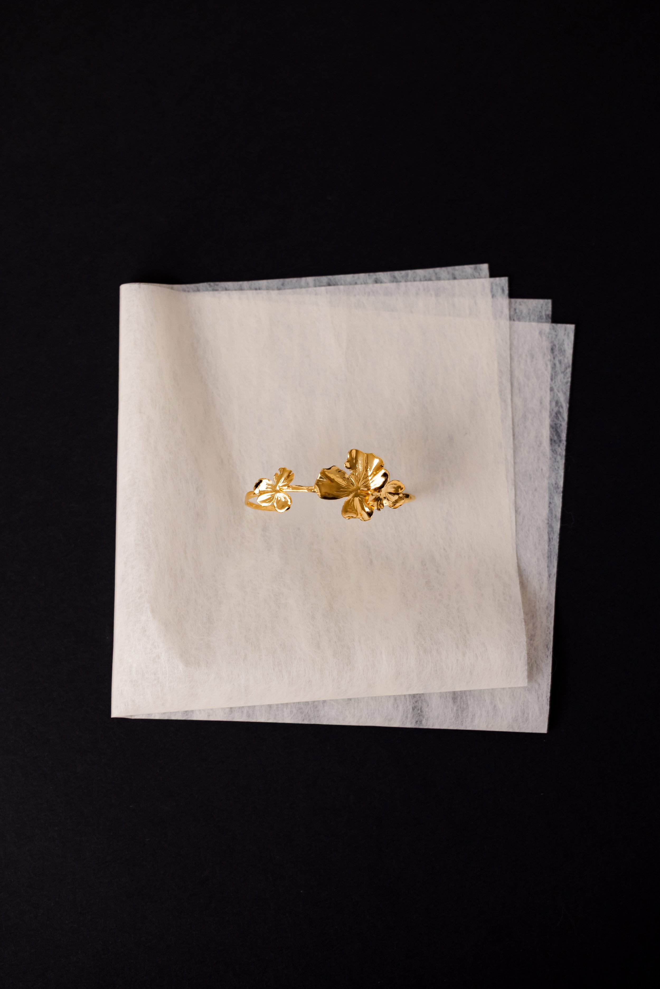 Bracelet floral en or sur fond noir et posé sur une feuille beige