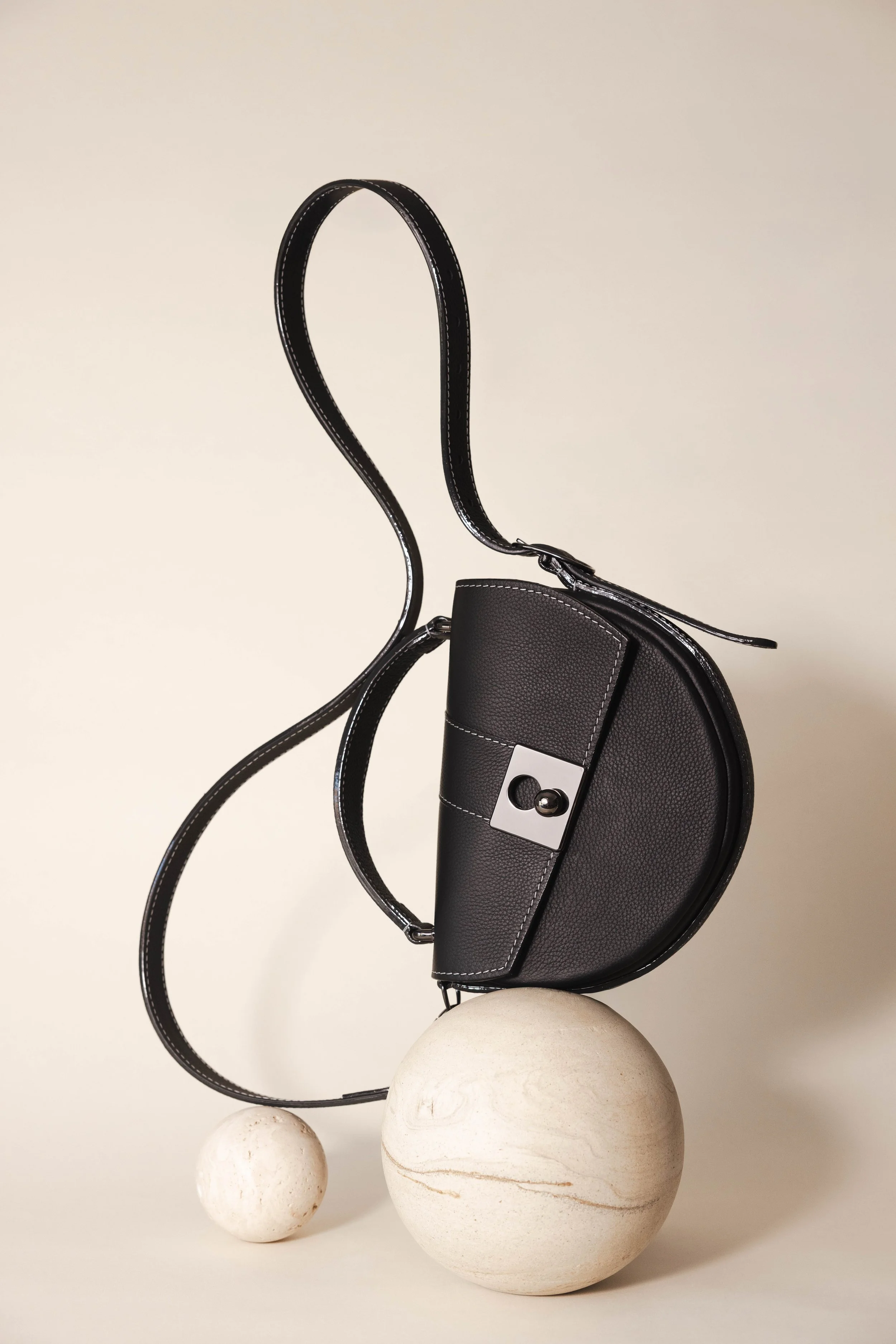 Sac en cuir noir posé en équilibre sur une boule en pierre, en studio sur fond neutre