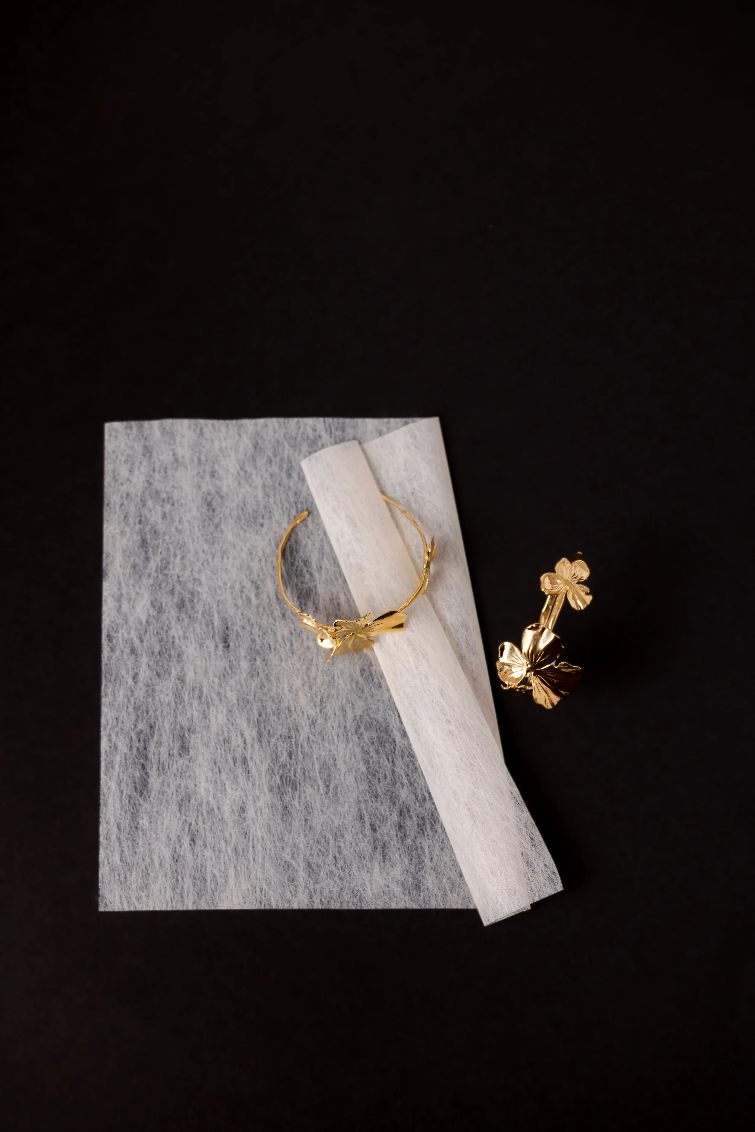 Boucle d'oreilles à motif floral en or posé sur une feuille ivoire elle même sur un fond noir