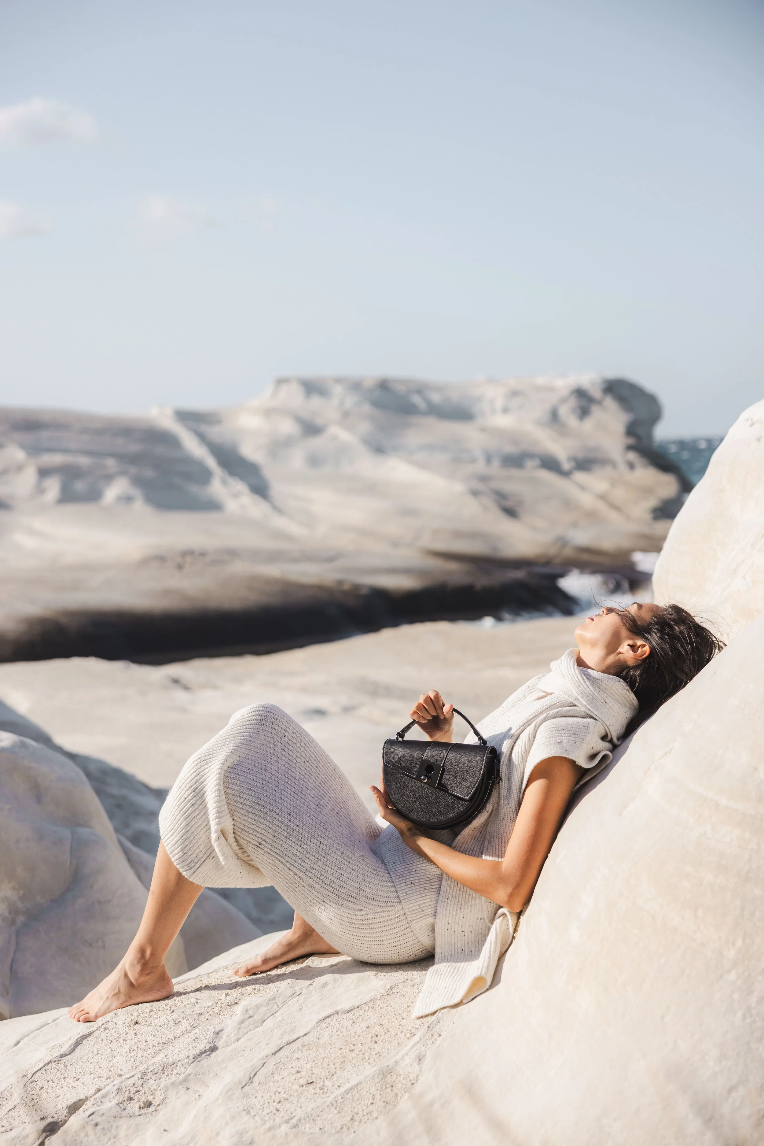 Photo d'une monde d'une femme allongée dans un décor lunaire et tenant un sac en cuir noir