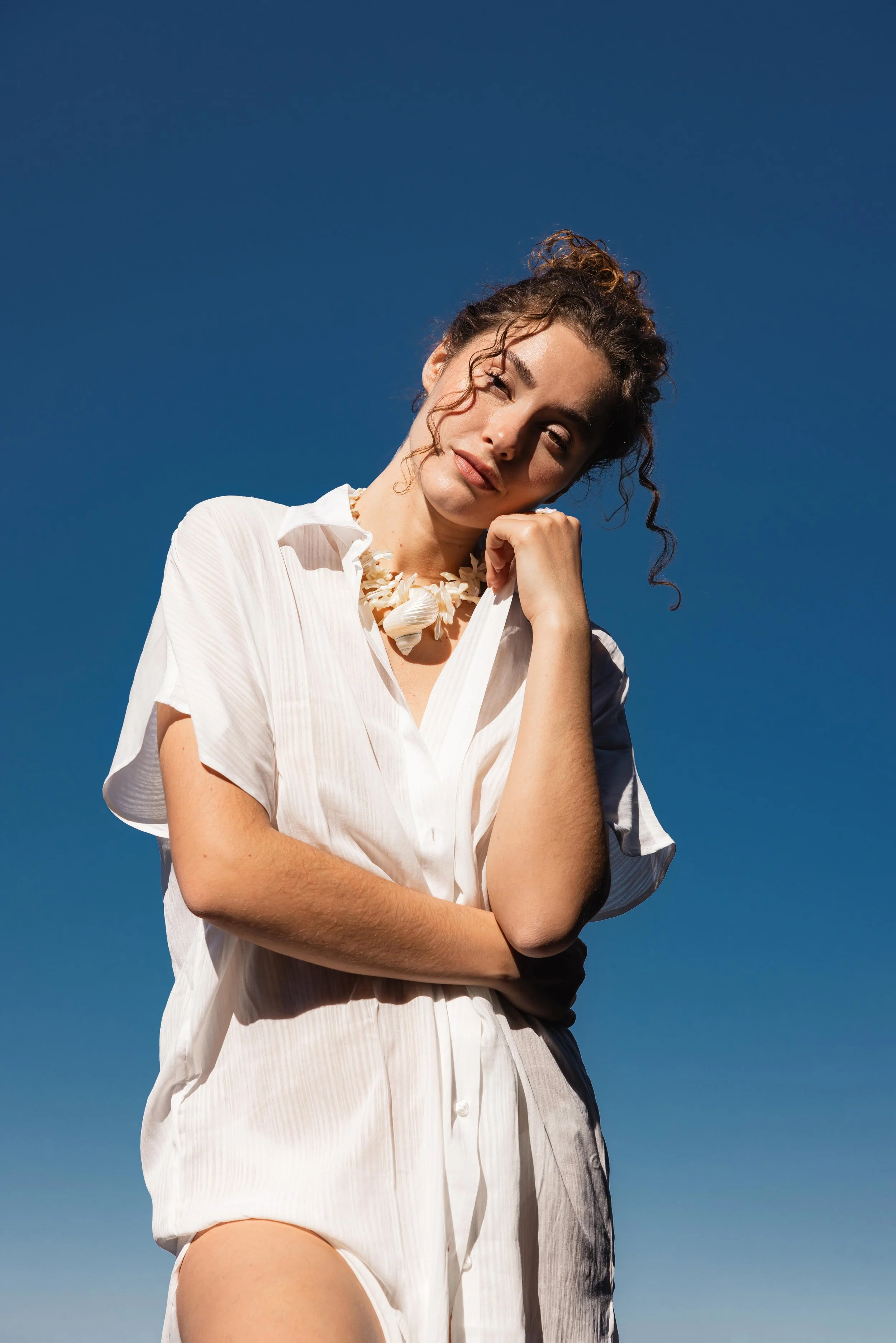 Portrait d'une mannequin en robe blanche et collier coquillage sur un fond de ciel bleu