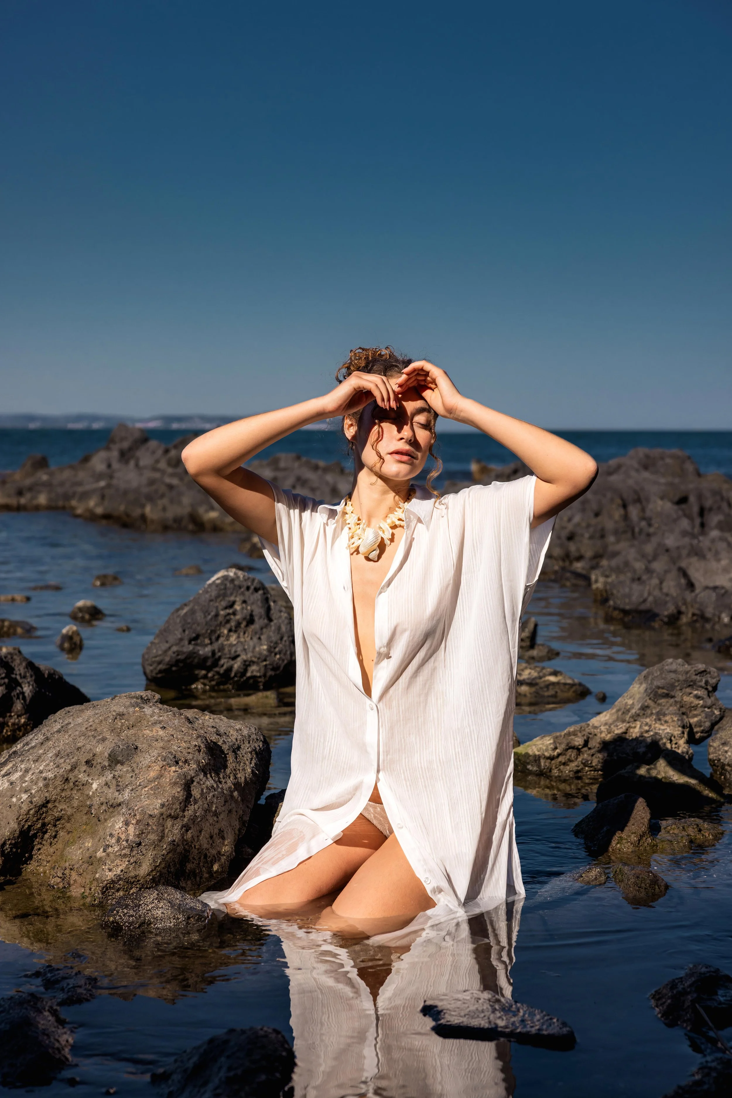 Mannequin posant assise dans l'eau et portant un collier coquillage sous un ciel bleu