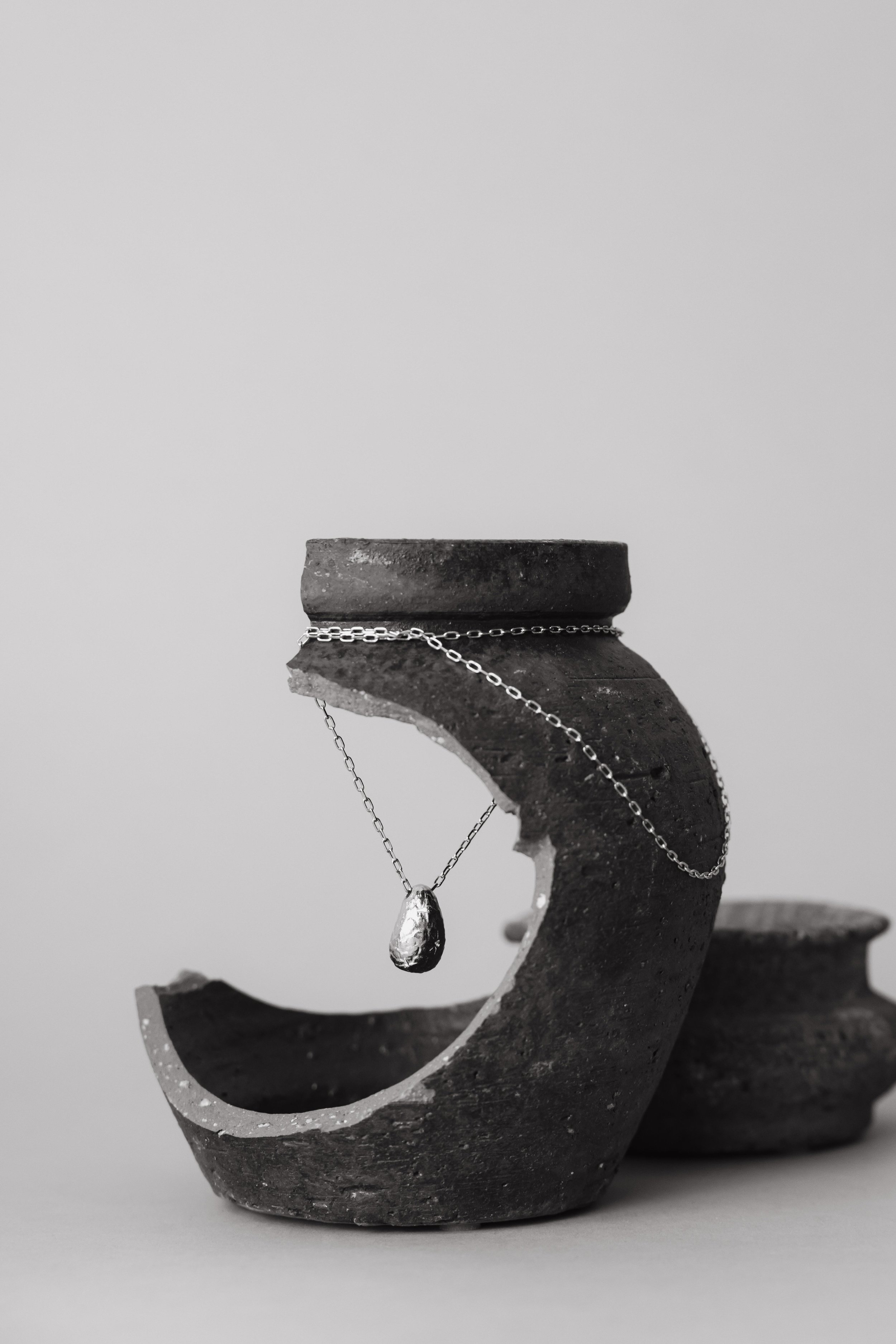 Nature morte en noir et blanc d'un collier en or posé sur une poterie cassée