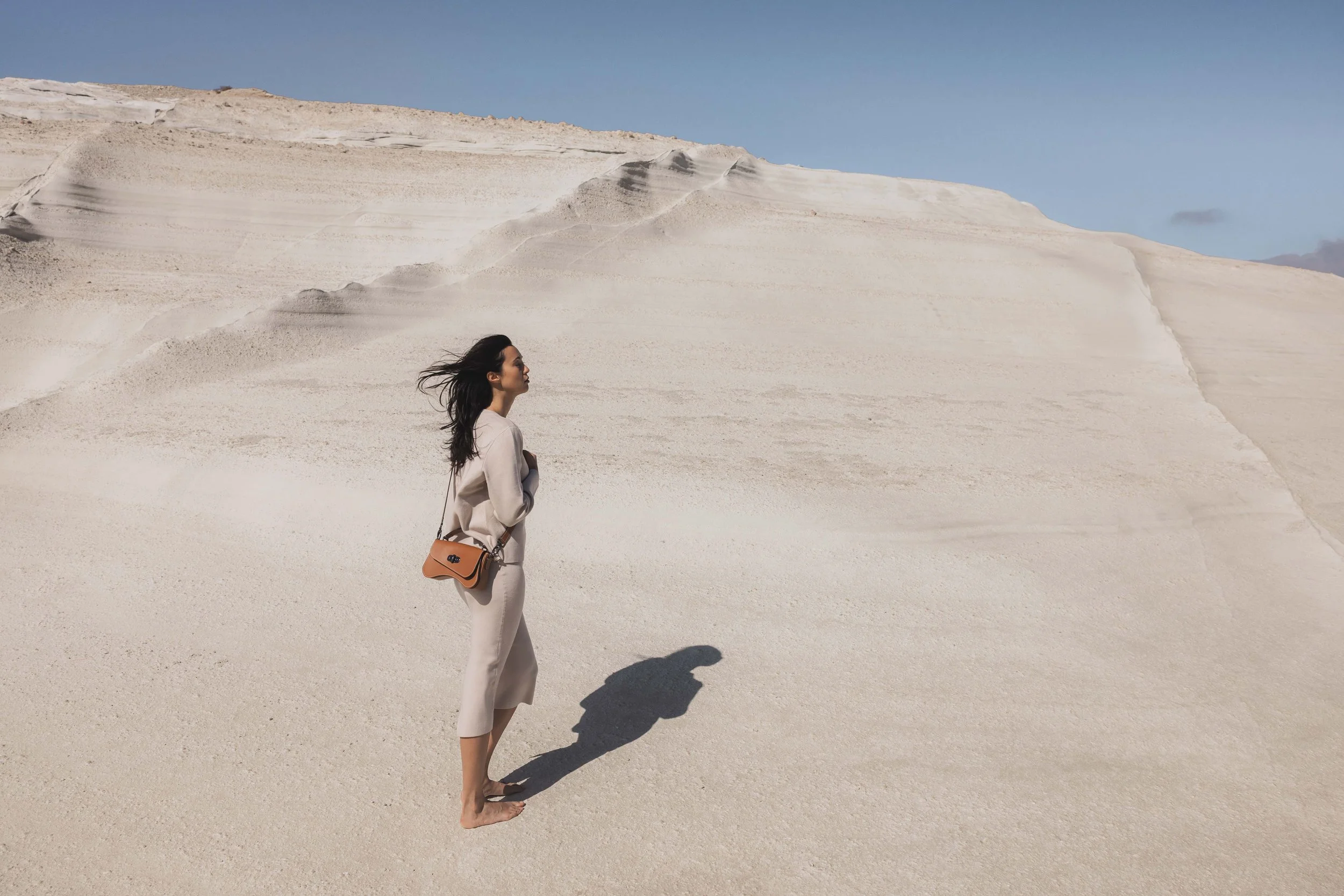Mannequin debout portant un sac en cuir dans un paysage désertique sous lumière naturelle