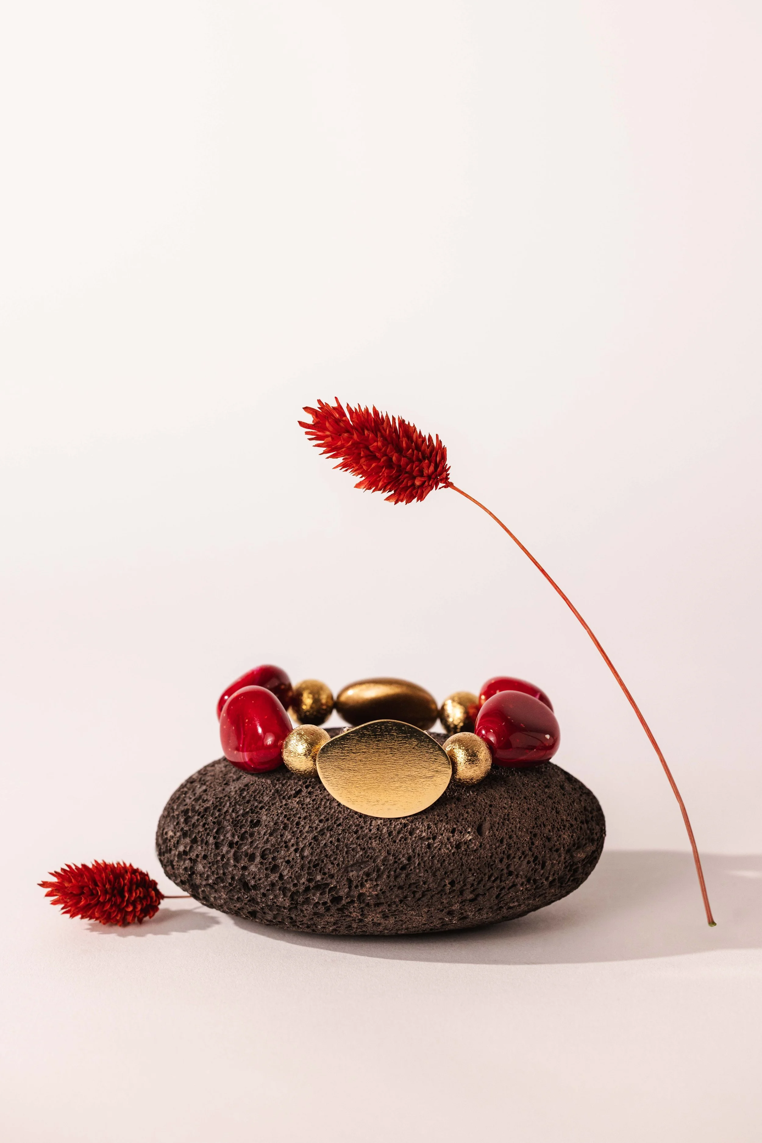 Nature morte minimaliste d'un bracelet en pierres rouges posé sur une pierre noire
