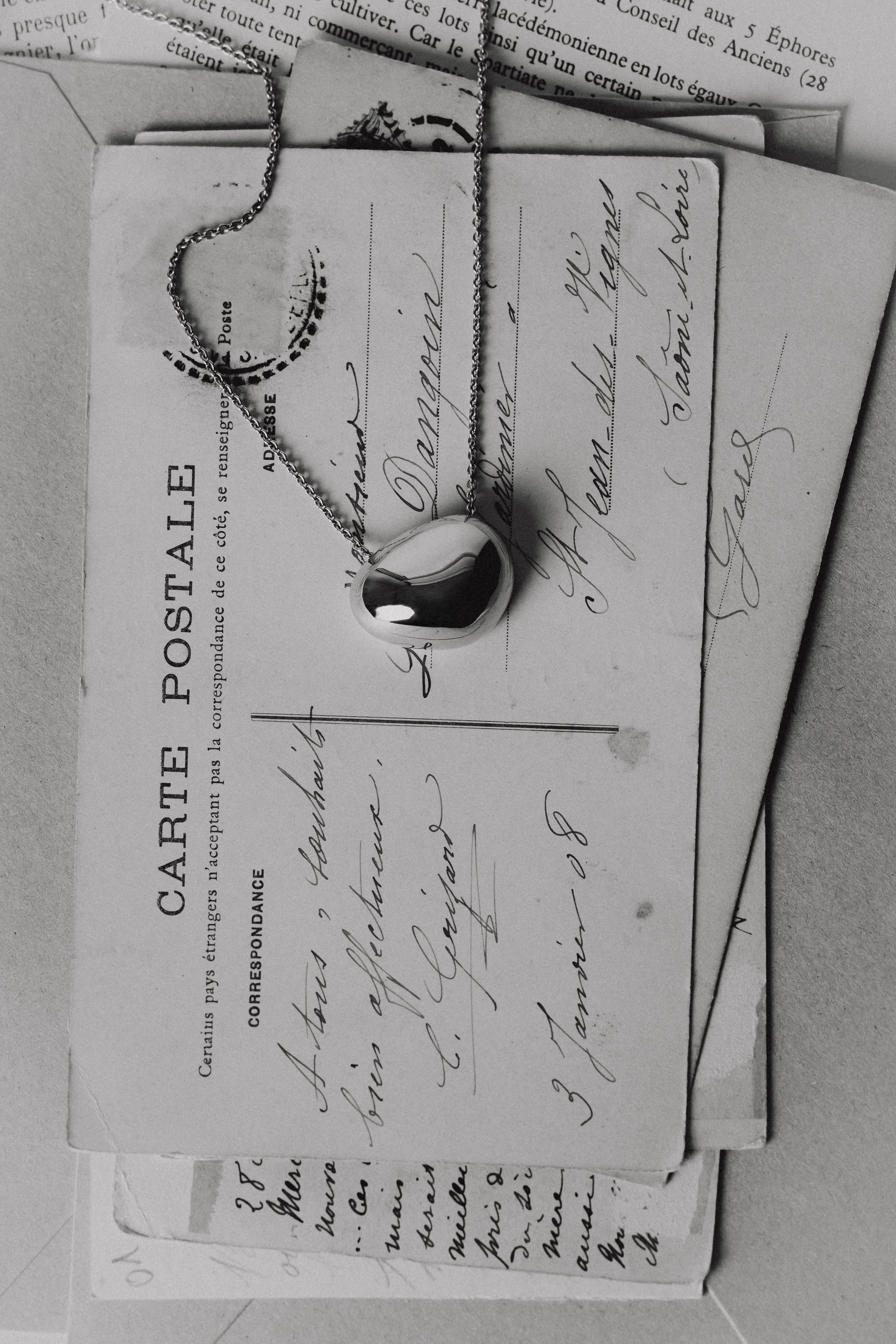 Photo en studio d'un collier en or posé sur une pile de cartes postales anciennes