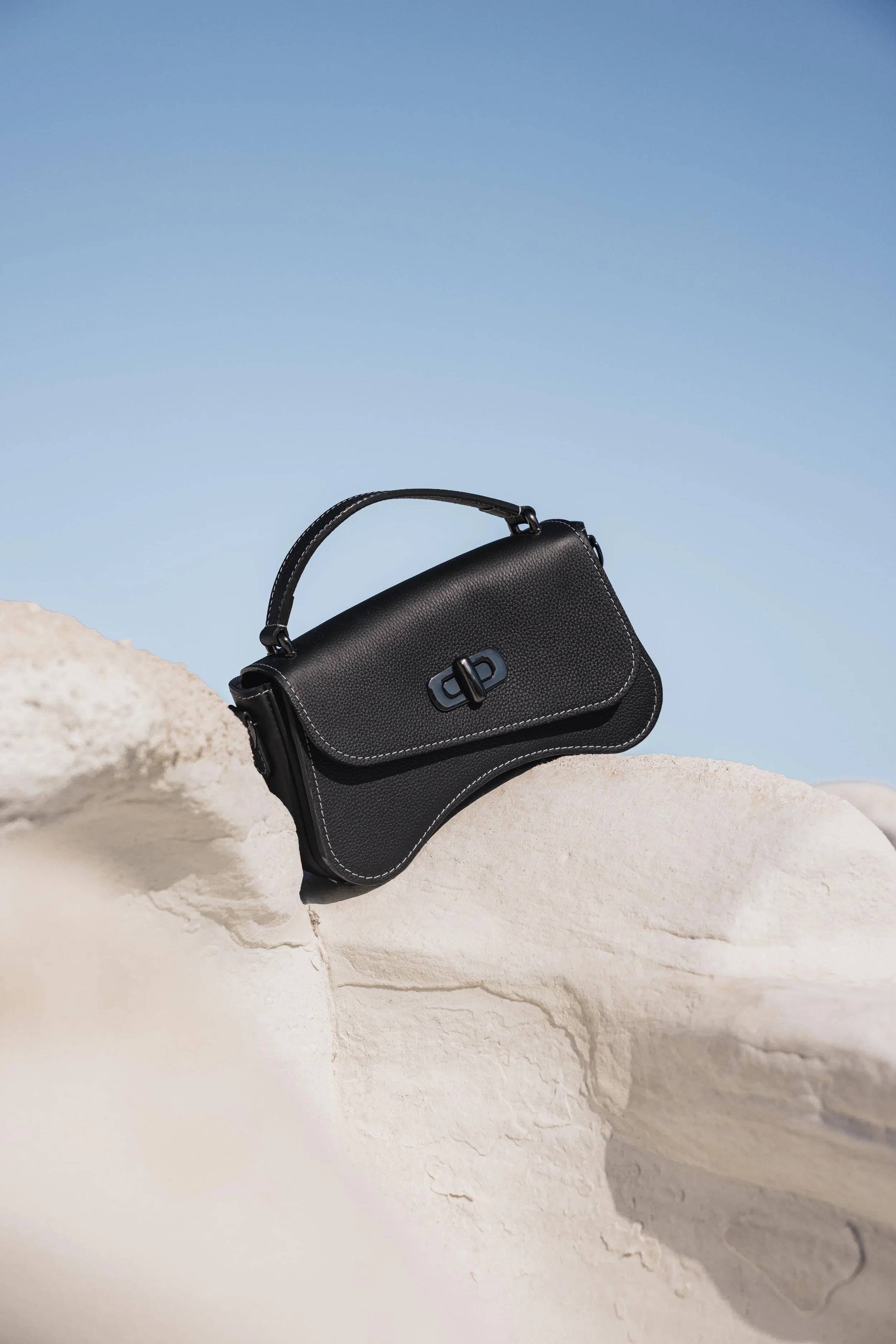 Sac en cuir noir posé sur une roche blanche sous un ciel bleu