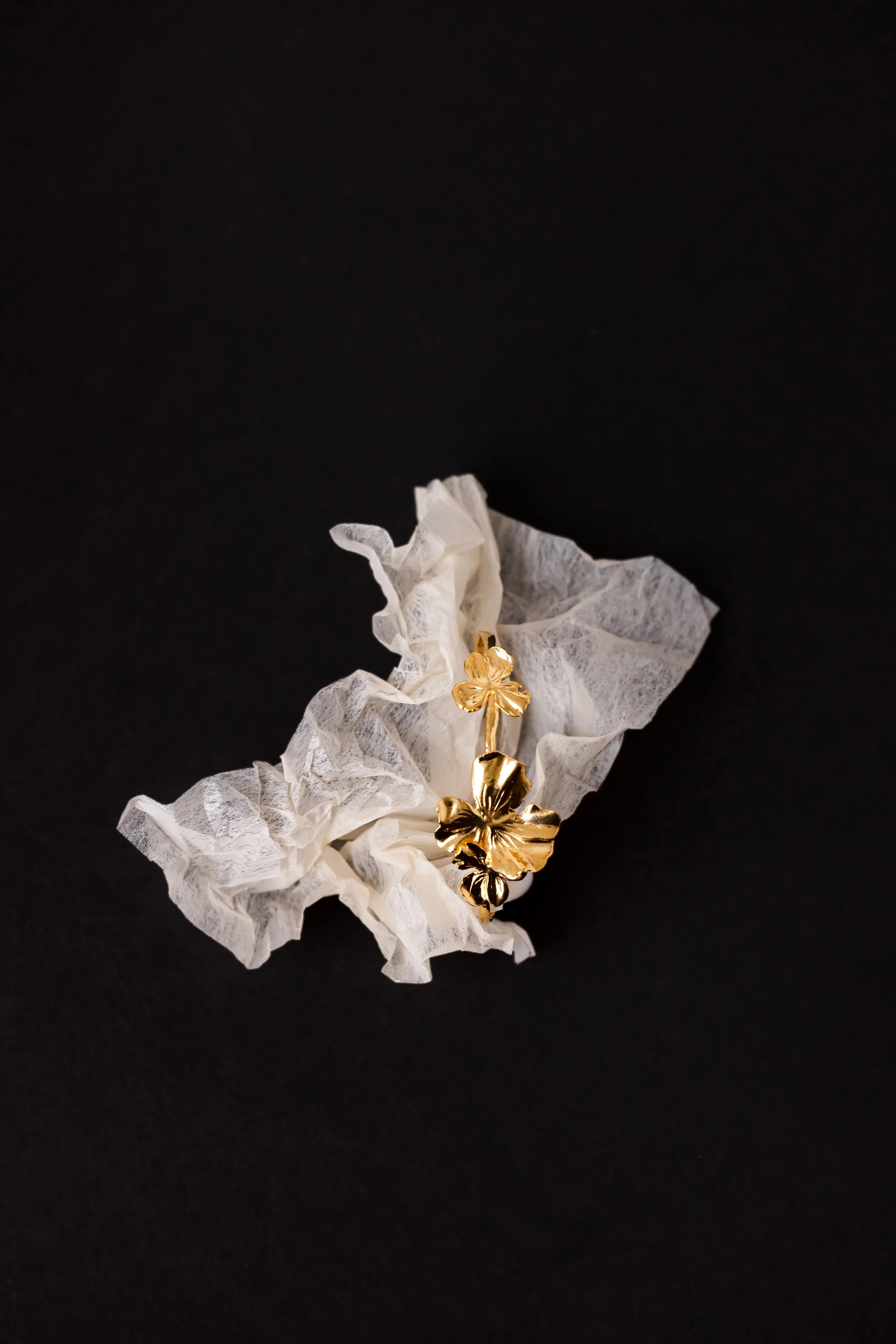 Bracelet jonc en or posé sur une feuille blanche froissée sur fond noir