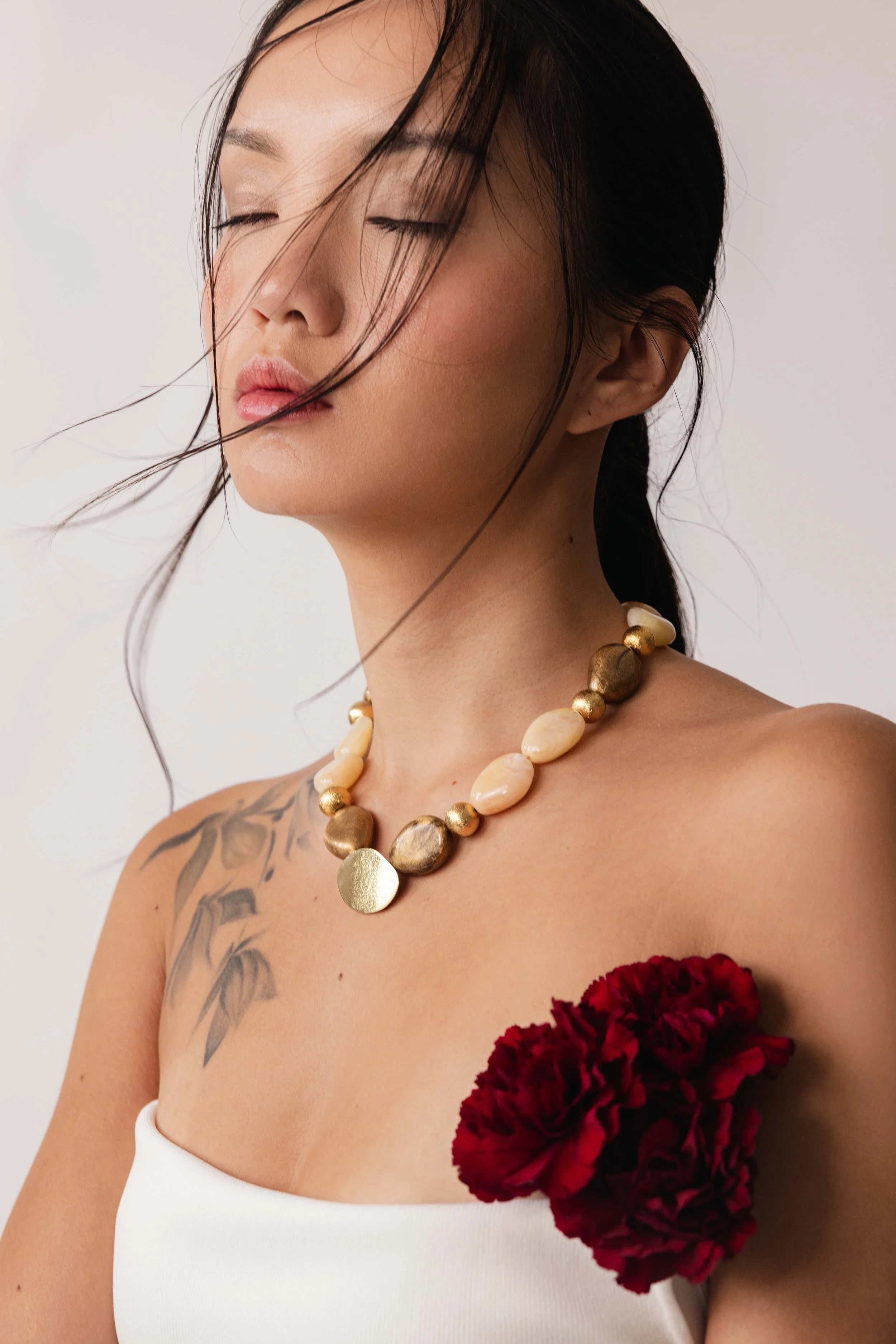 Portrait épuré d'une mannequin portant un gros collier en pierres et une fleur sous son bras 