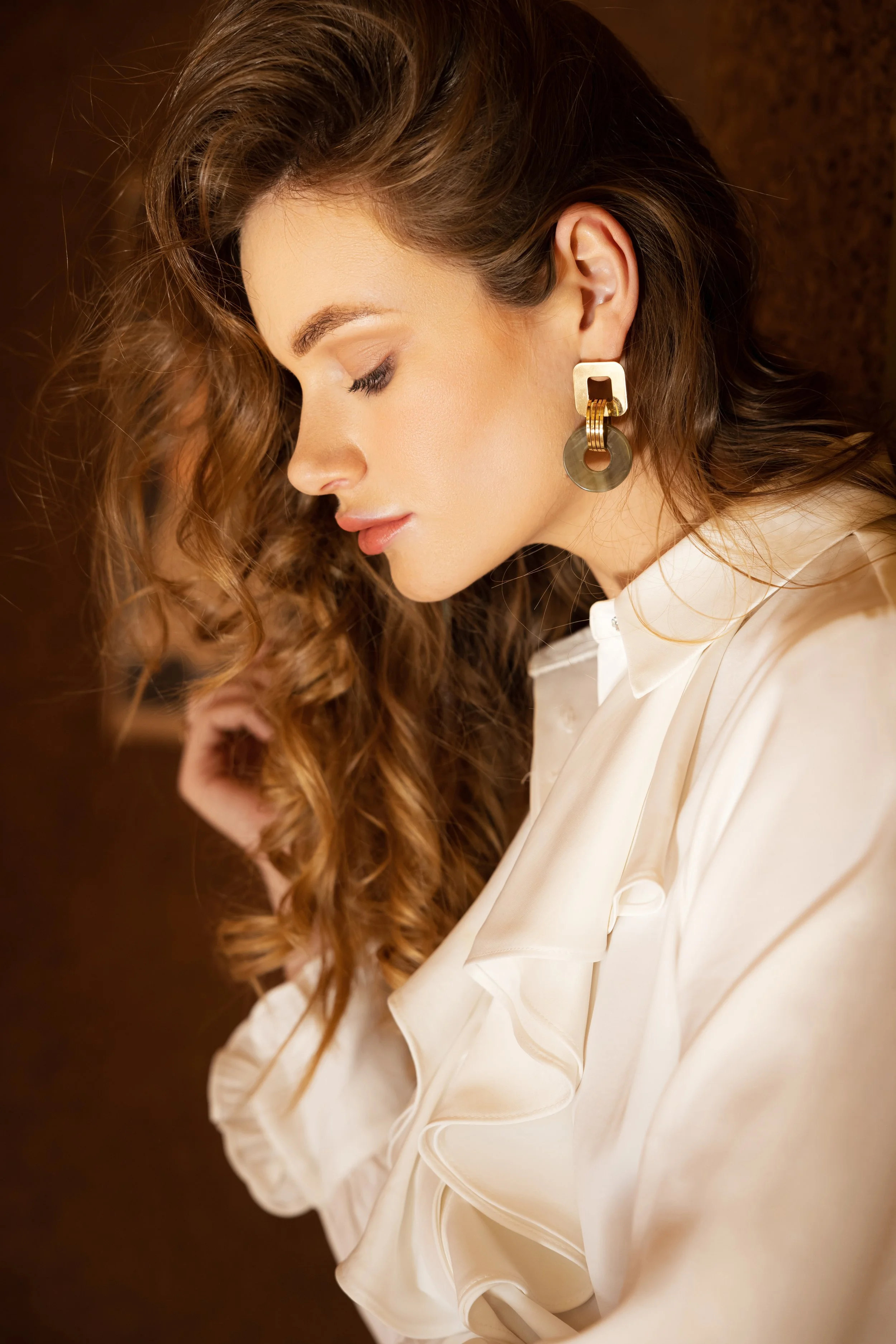 Portrait d'une mannequin aux cheveux bouclés avec une boucle d'oreille sur fond marron