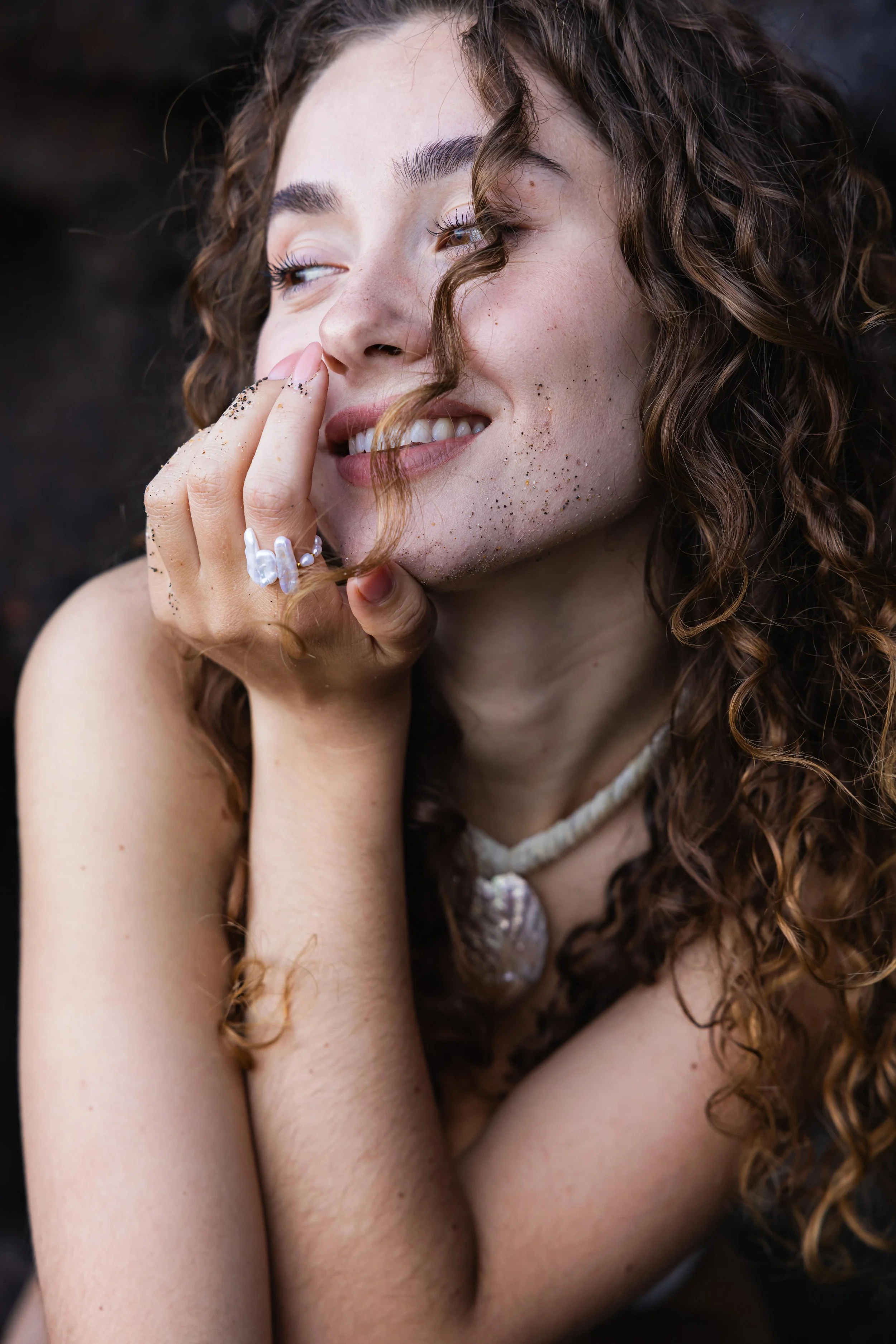 Portrait serré d'une mannequin avec bague coquillage sur une plage noire ensoleillée