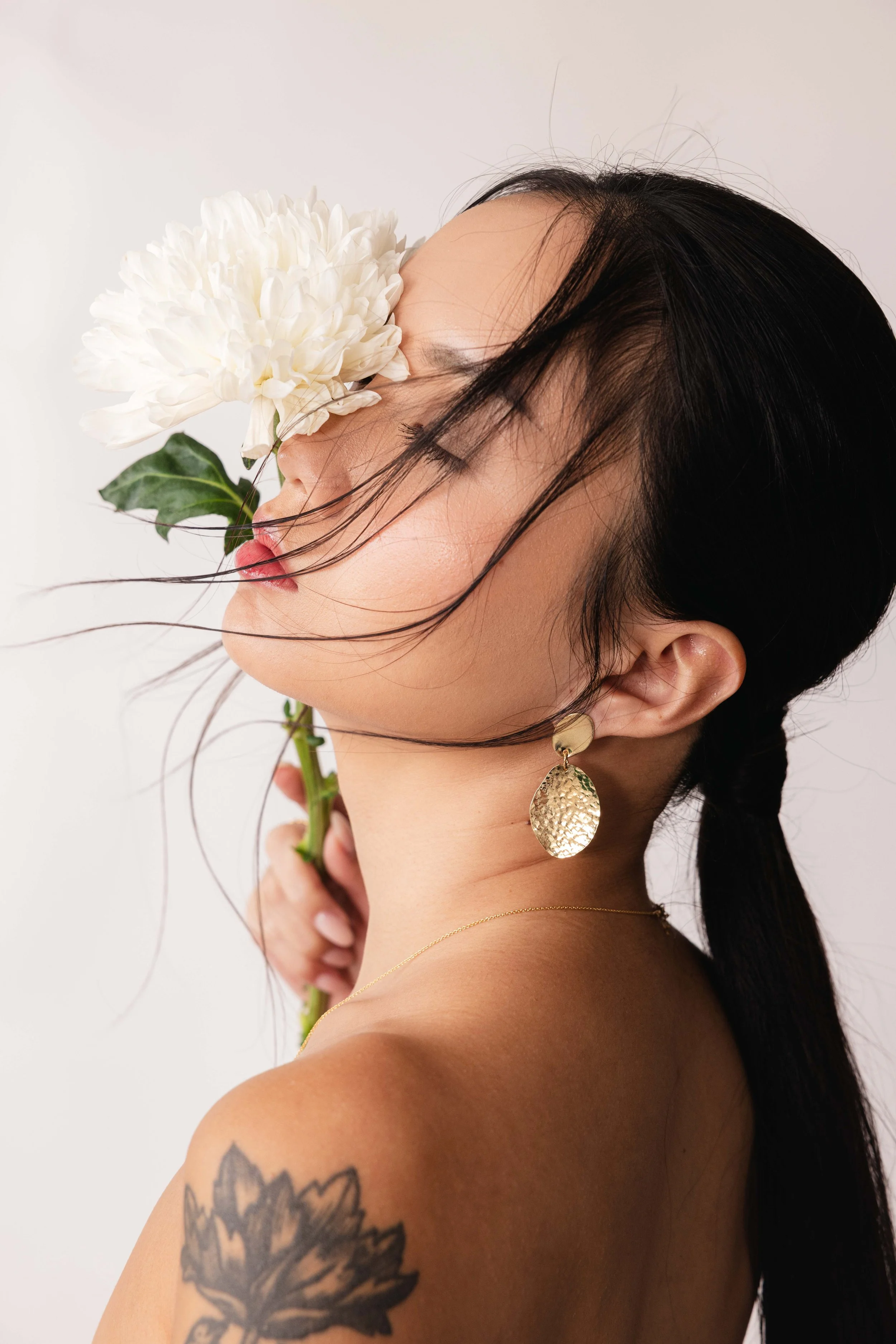 Portrait d'une mannequin avec une fleur sur son visage et une boucle d'oreille en or