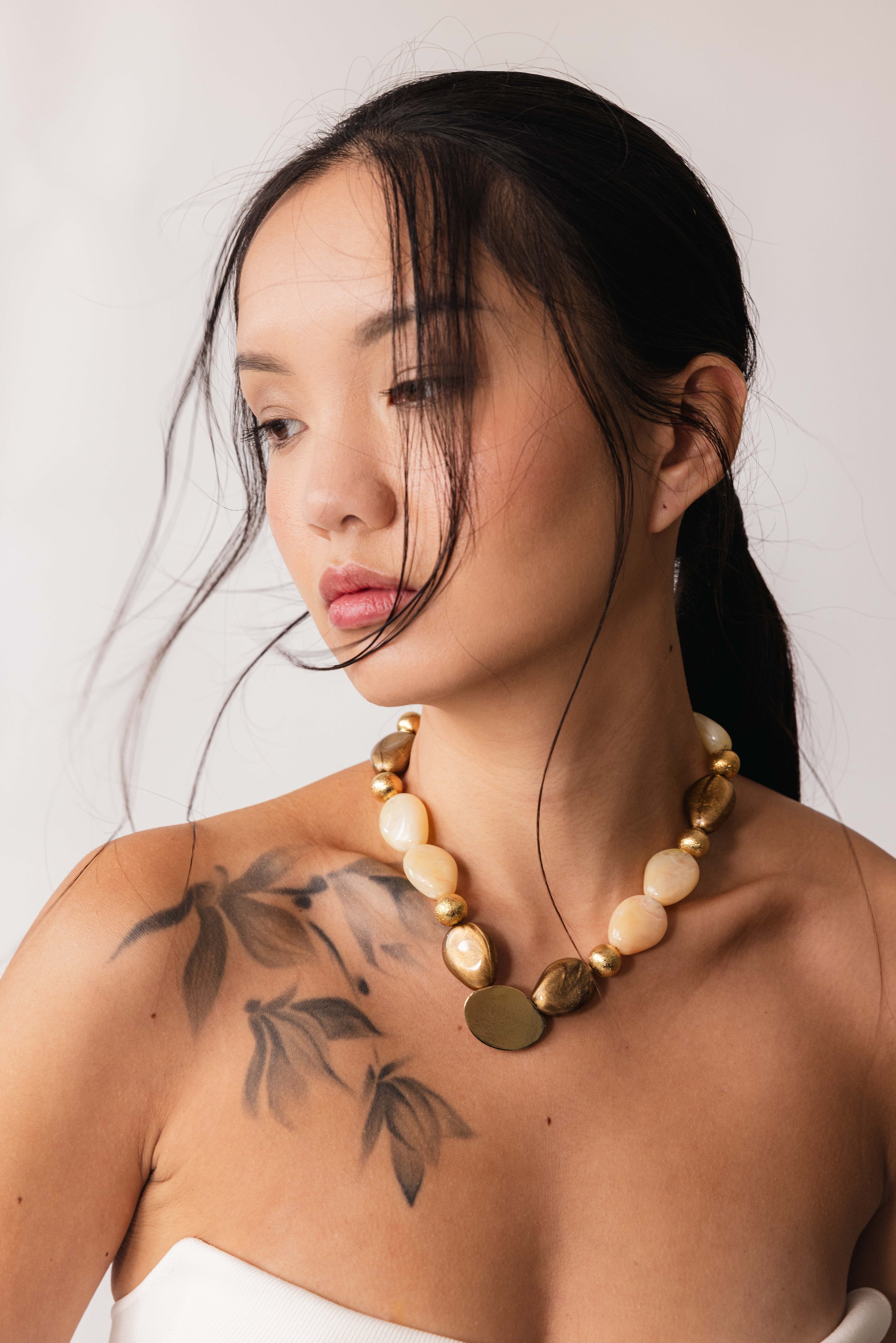 Portrait minimaliste d'une mannequin tatouée portant un gros collier en pierres