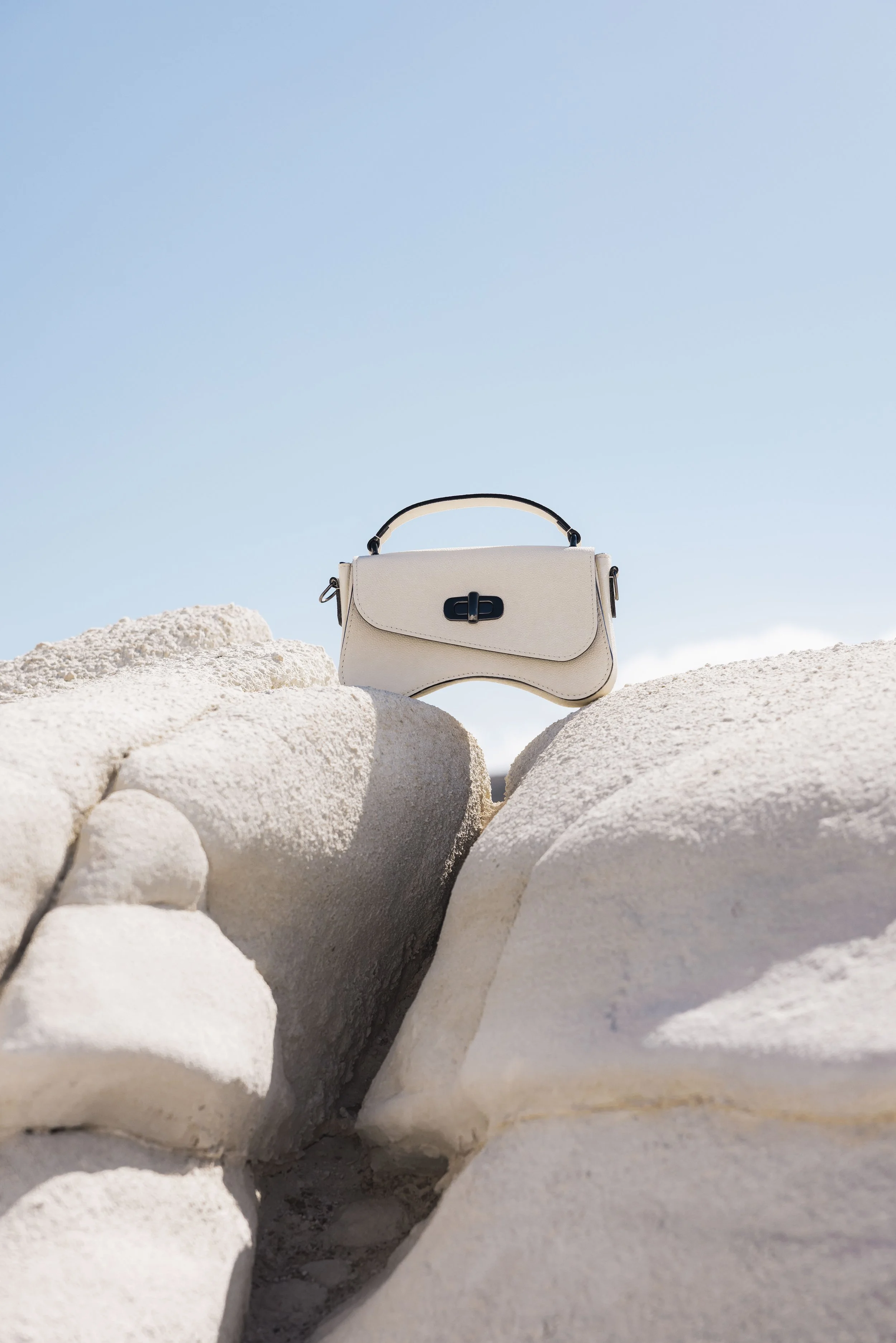 Sac blanc en cuir blanc posé sur une paroi minérale blanche contrastant avec le bleu du ciel