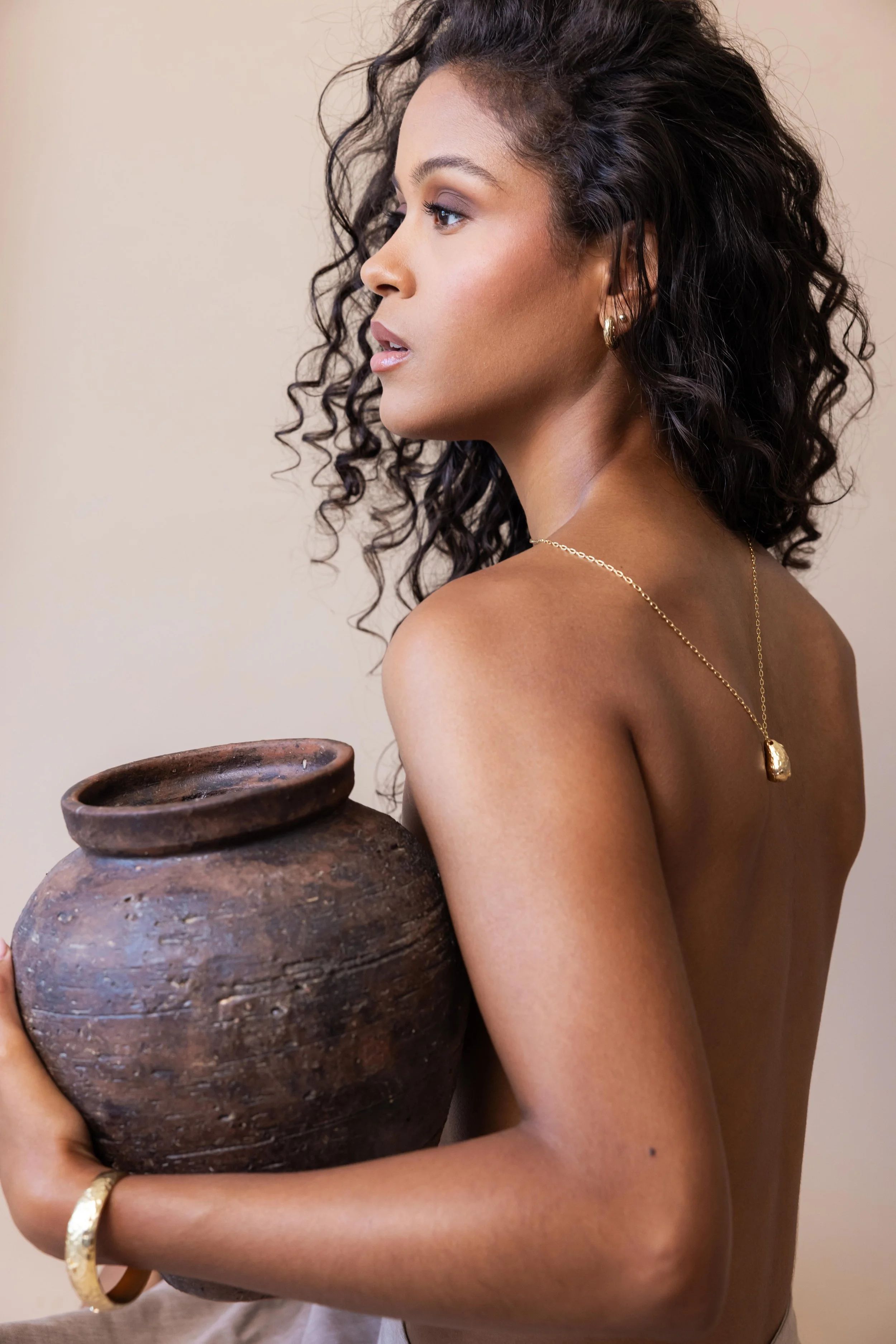 Mannequin portant un collier en or sur son dos nu et tenant dans ses bras une poterie