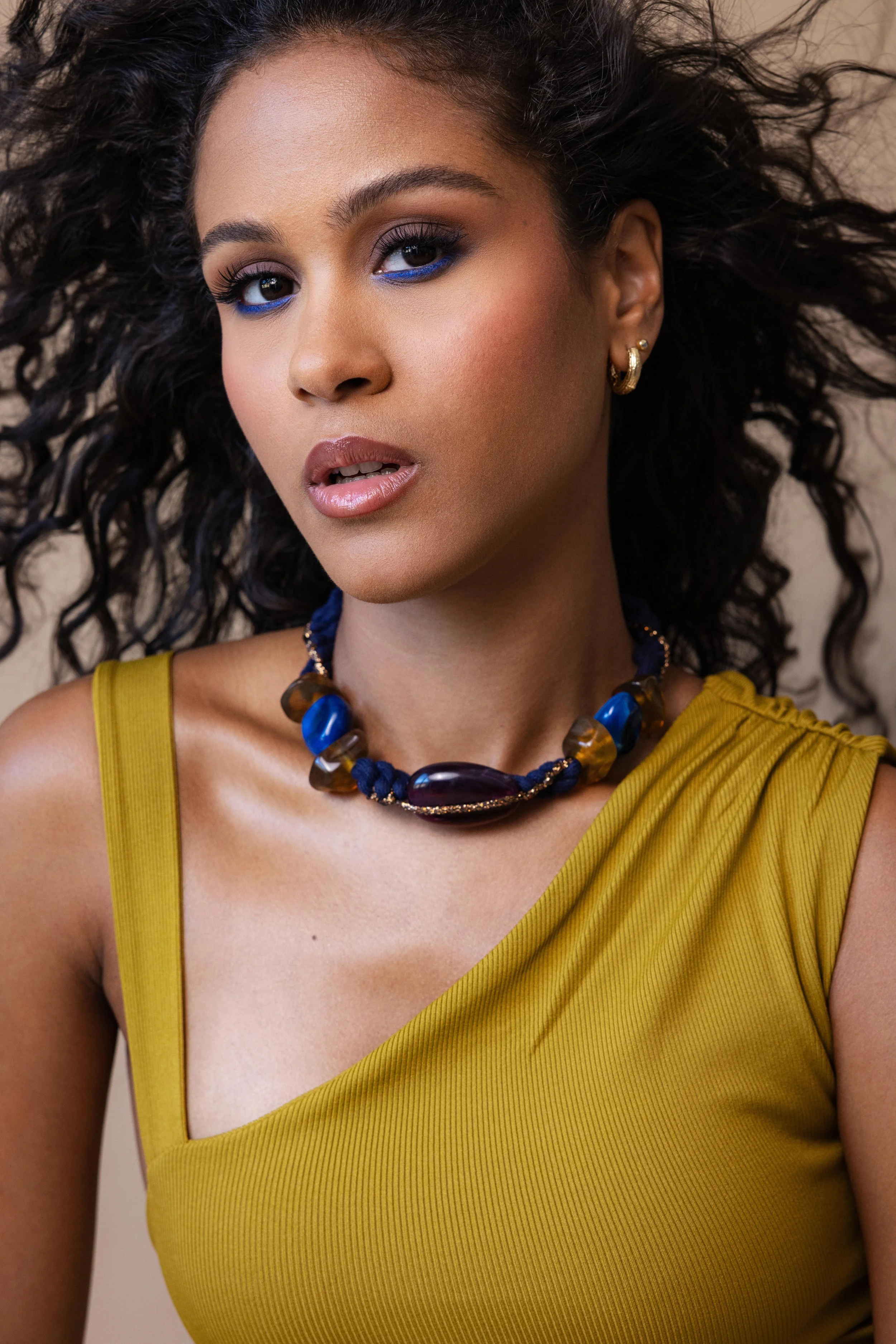Portrait serré en studio d'une mannequin portant une robe jaune et un collier en pierres bleues
