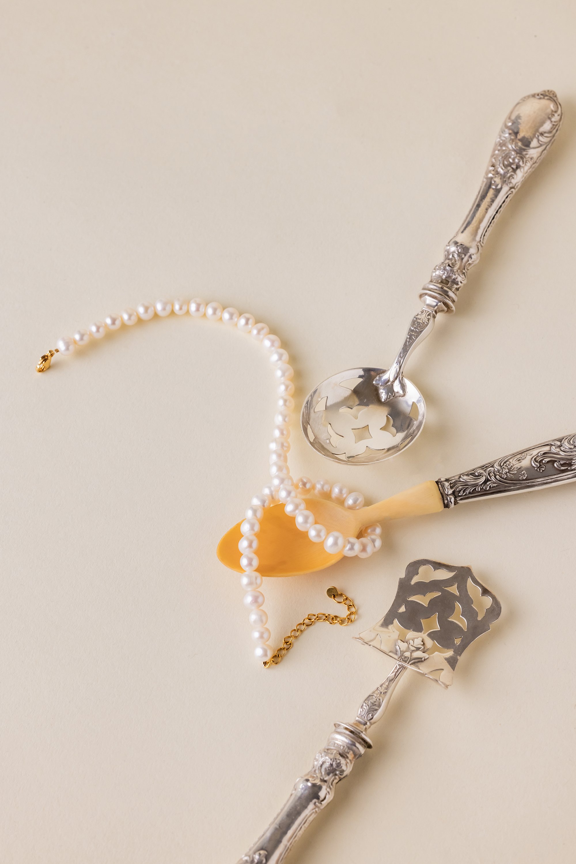 Nature morte d'une bracelet en perles posé sur des couverts anciens en argent